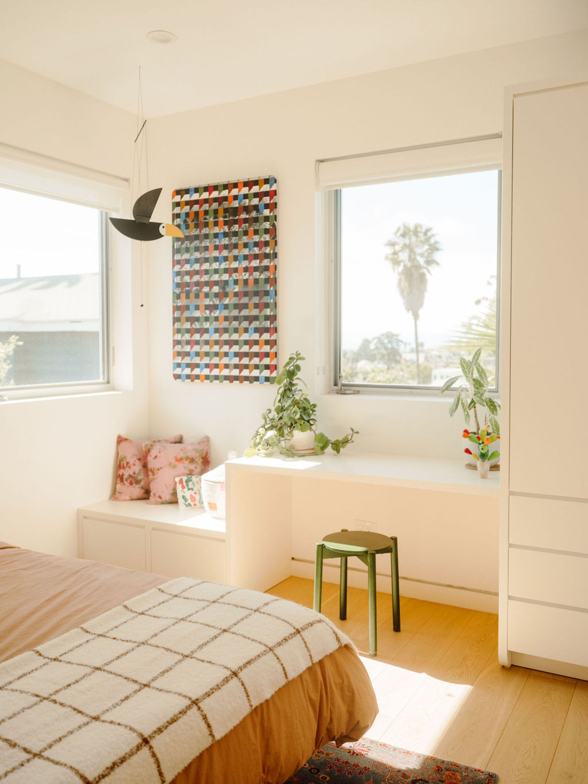 Bedroom view toward the built-in desk and bench, with a hanging bird mobile and a palm visible through the window