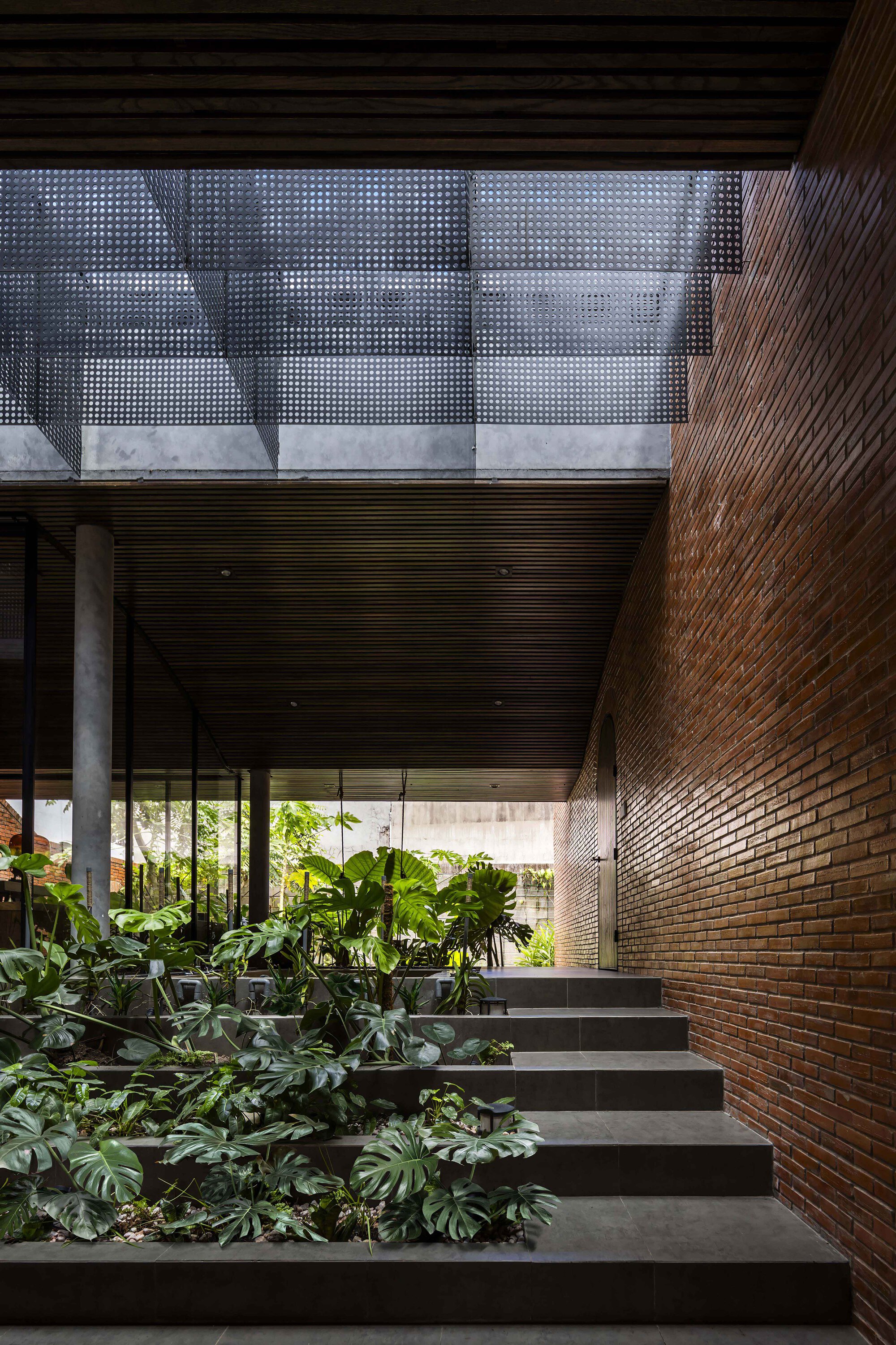 Low stone steps planted with monstera beside a tall brick wall, beneath a perforated metal screen and slatted timber soffit