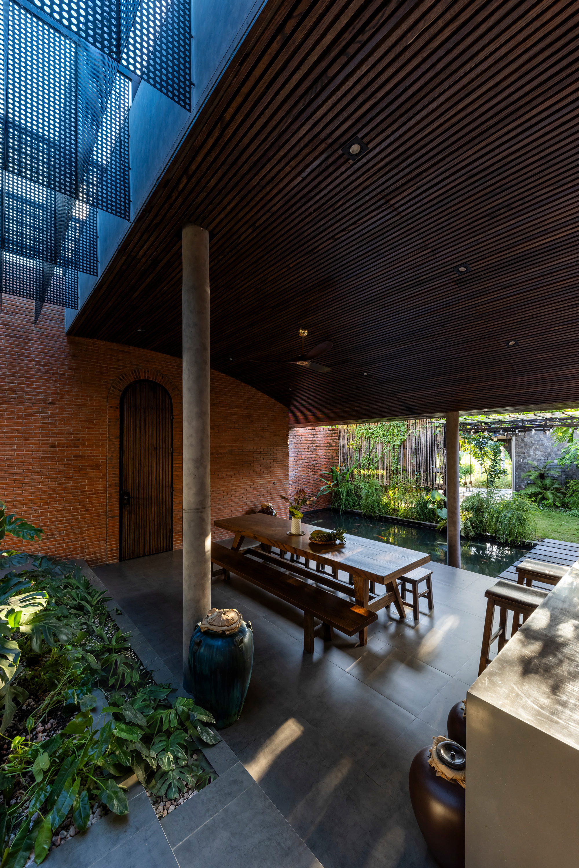 Covered dining area with arched timber door in a curved brick wall, ceramic jars and sunlight patches on the stone floor