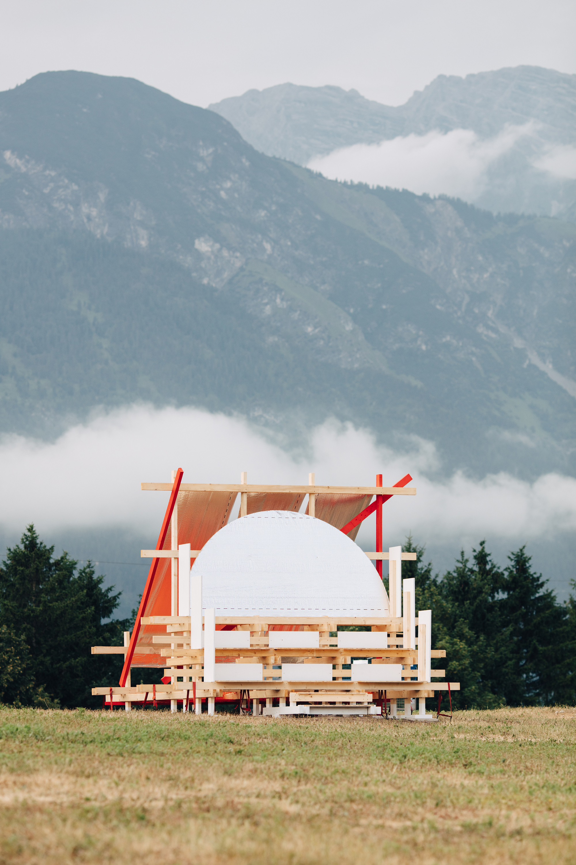 Front view of the timber stack and white dome with red struts, backed by steep mountains and low clouds