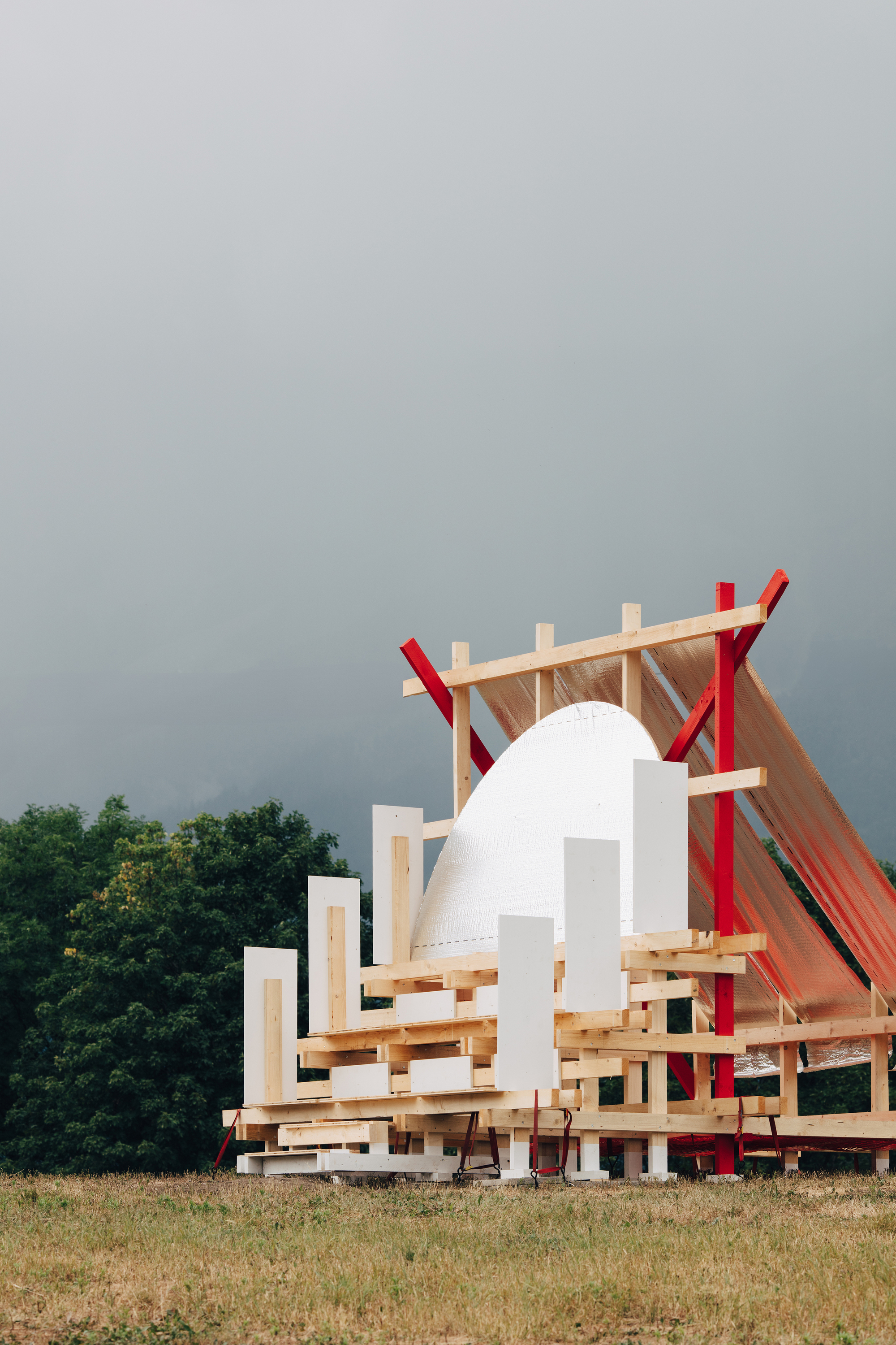 Side view of the stepped timber platform, white upright panels and red column under a dark stormy sky