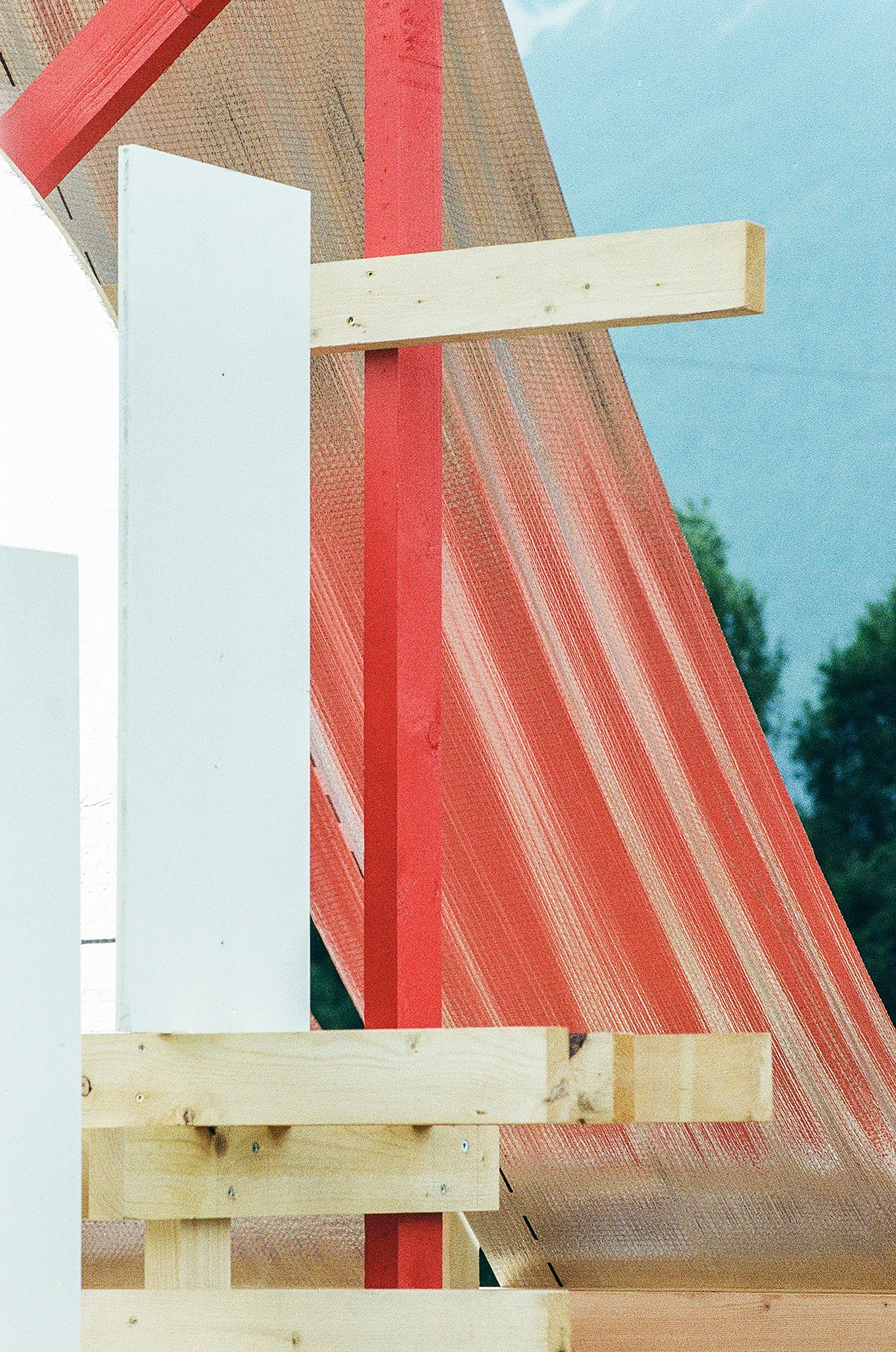 Red timber post and white panel against a translucent orange curved membrane, with green trees and blue hills behind