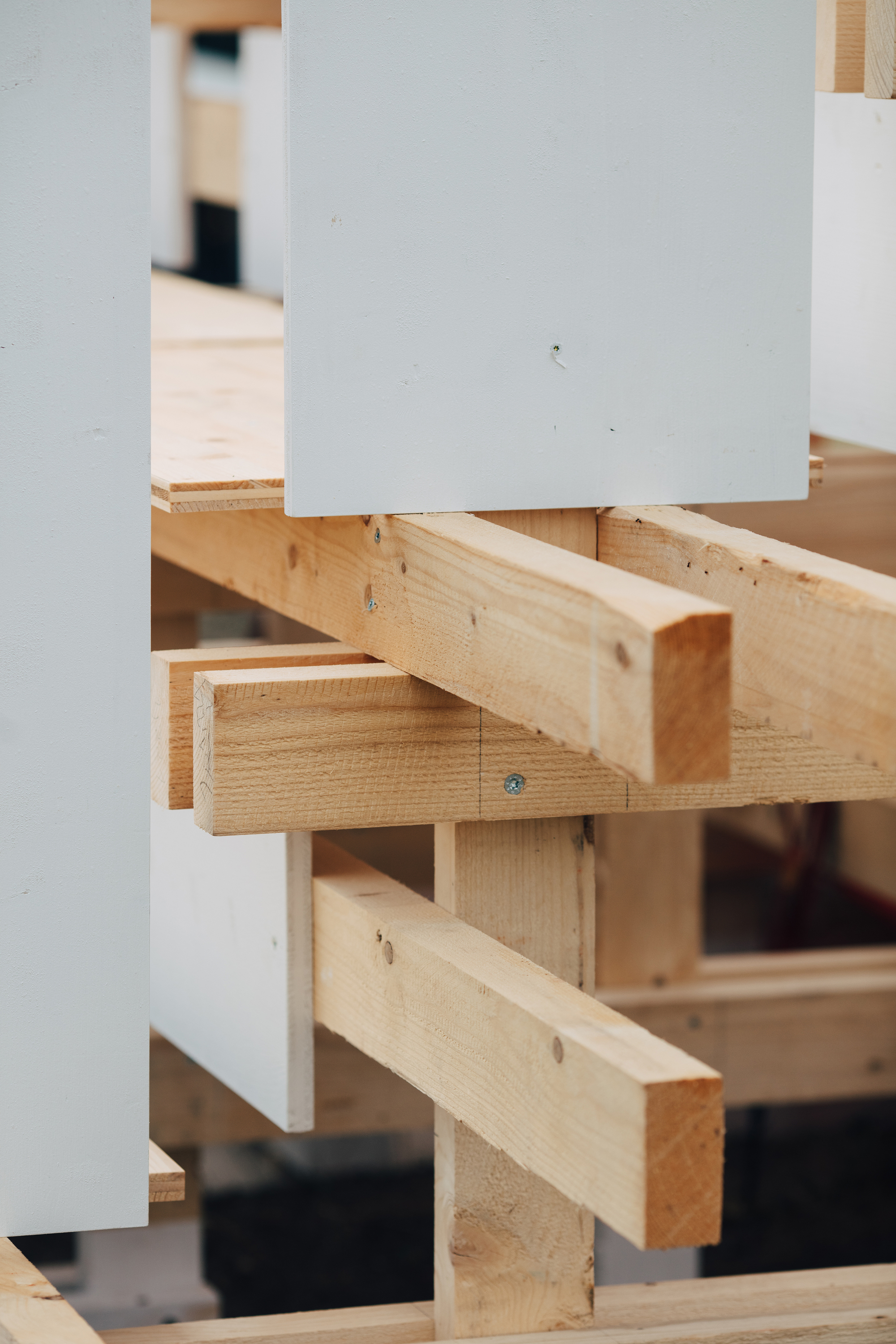 Close-up of overlapping timber beams joined with a single screw, beside white panels in soft daylight