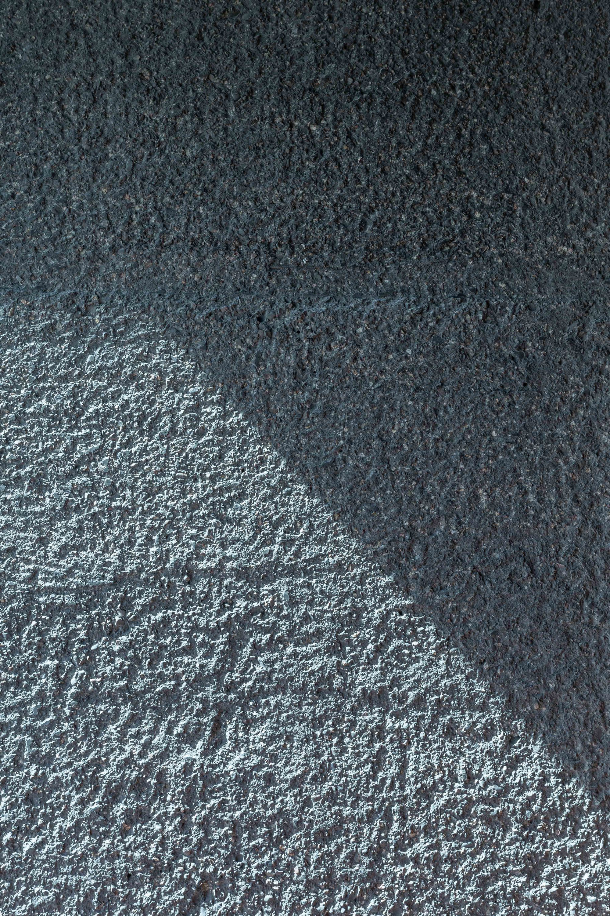 Close-up of rough gray plaster wall surface split diagonally by a sharp shadow edge