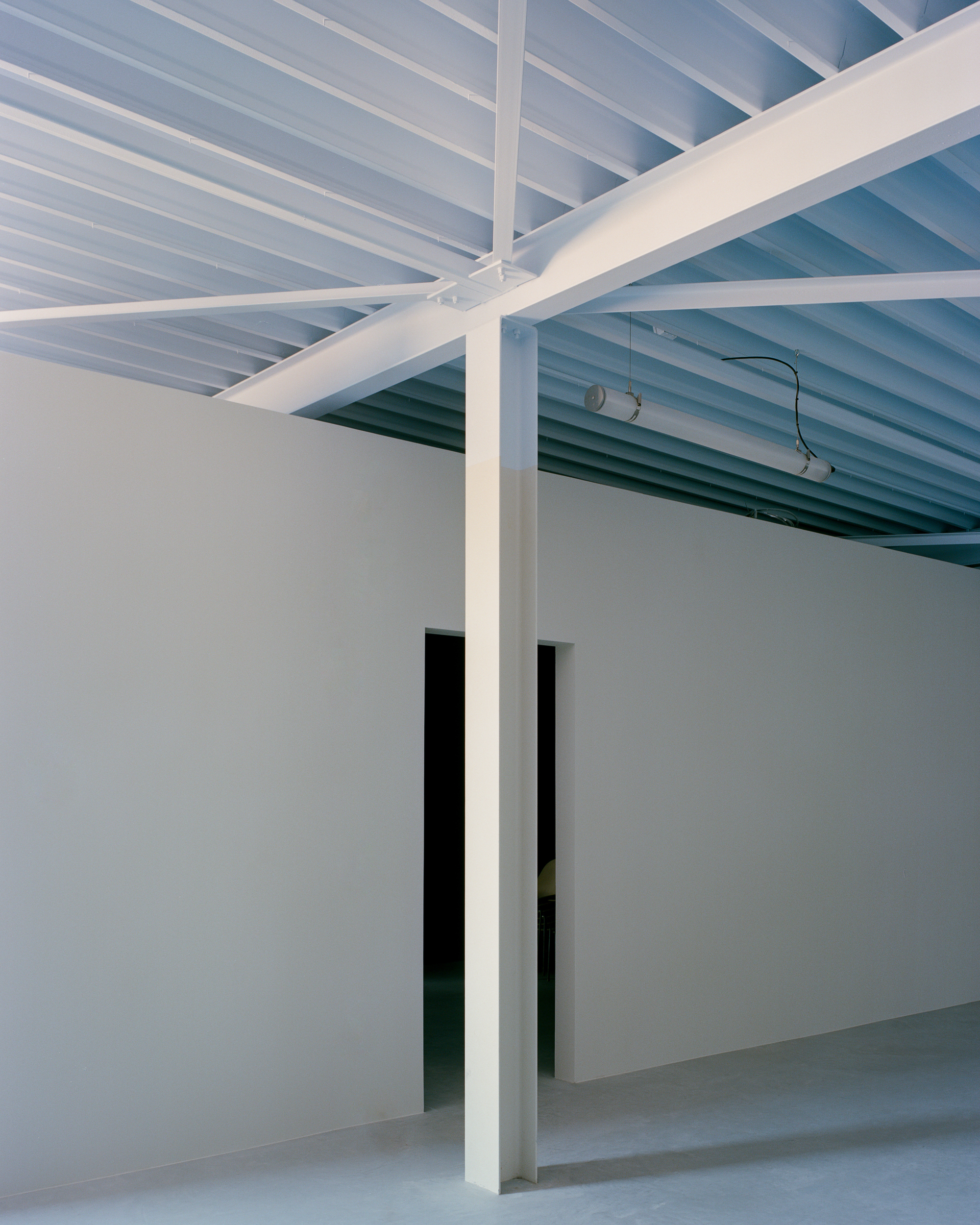 White steel column and beams under a ribbed ceiling, beside a partition wall with a dark doorway opening