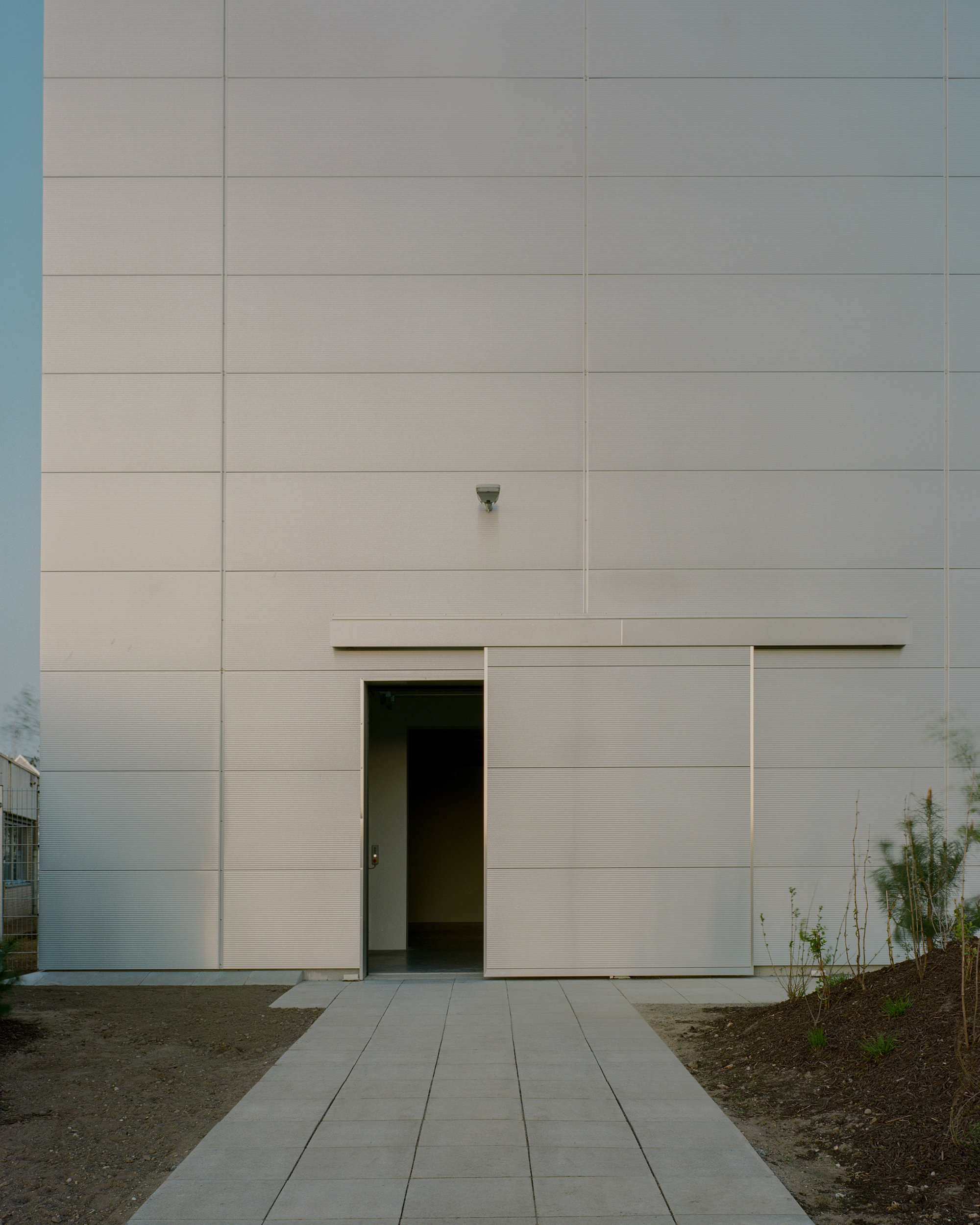 Frontal view of the panelled wall with an open sliding door at the end of a paved path, seen in soft evening light