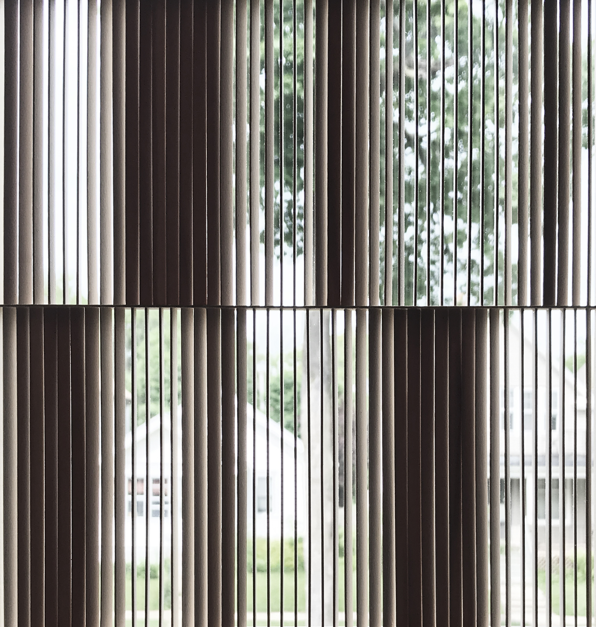 Close-up of vertical timber slats in offset panels, with a tree and a neighbouring white house visible through the gaps in daylight