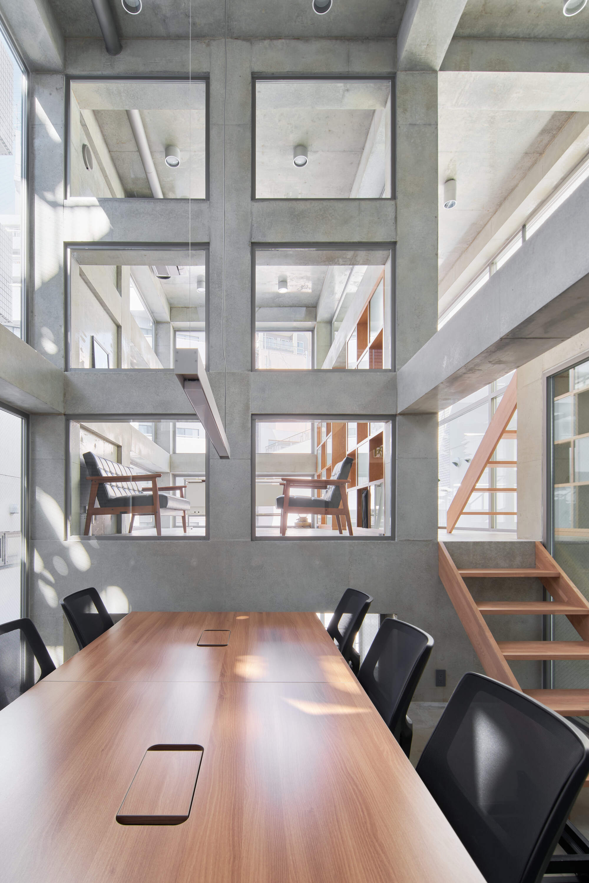 Timber conference table facing a concrete grid wall with square openings onto lounge chairs, with sunlight dappling the surface