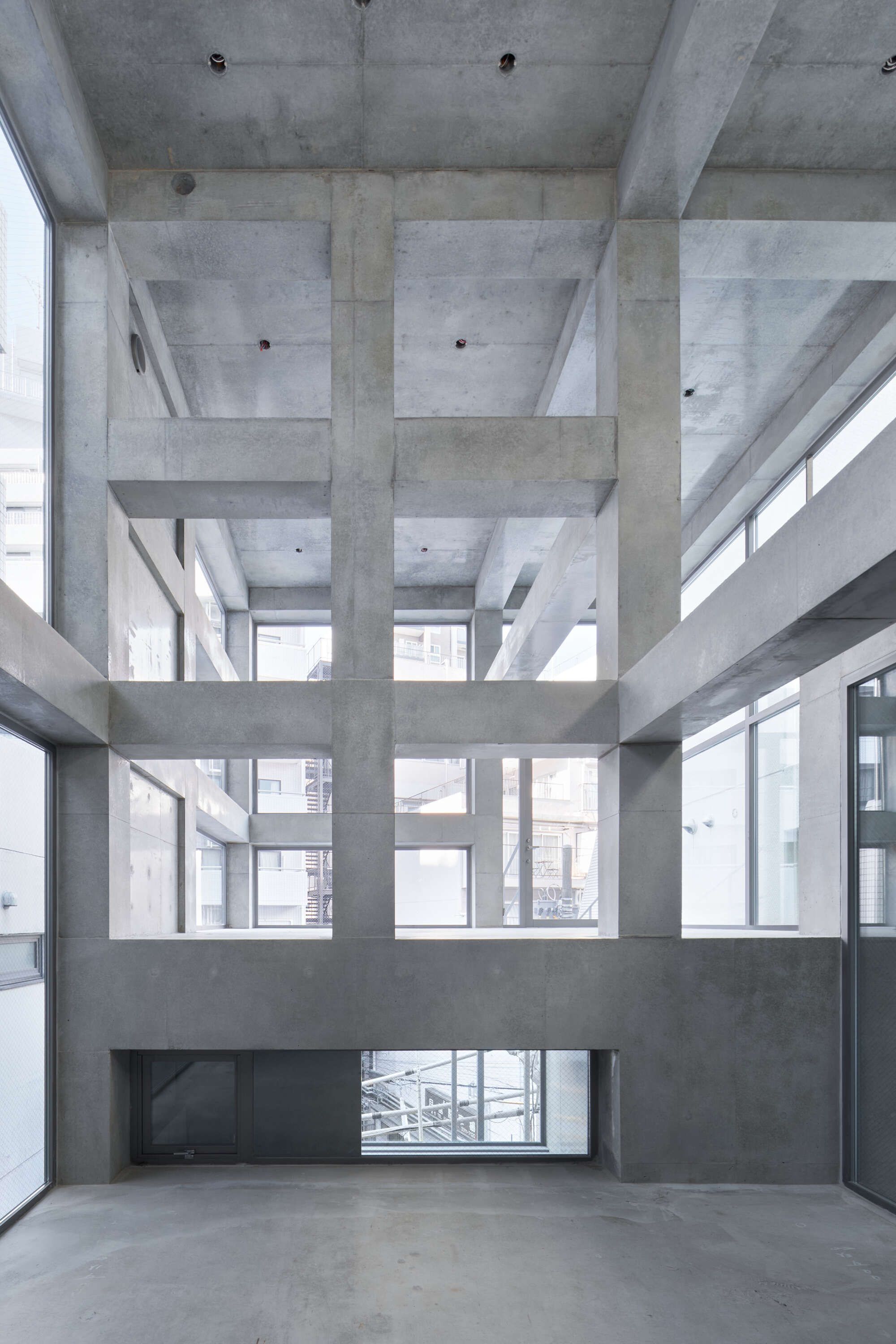 Double-height concrete interior with a grid of exposed beams and columns, daylight coming through high windows onto a bare floor