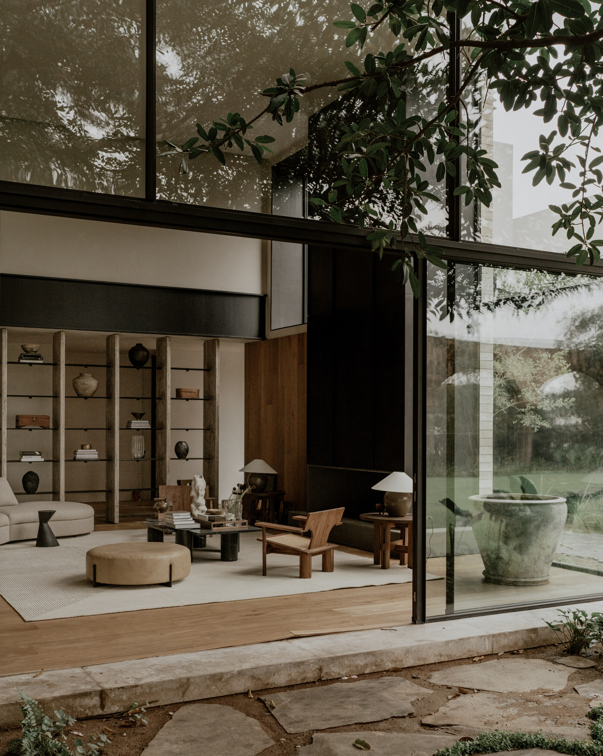 Living room opening through sliding glass to a stone terrace, with a large weathered planter and leafy branches overhead