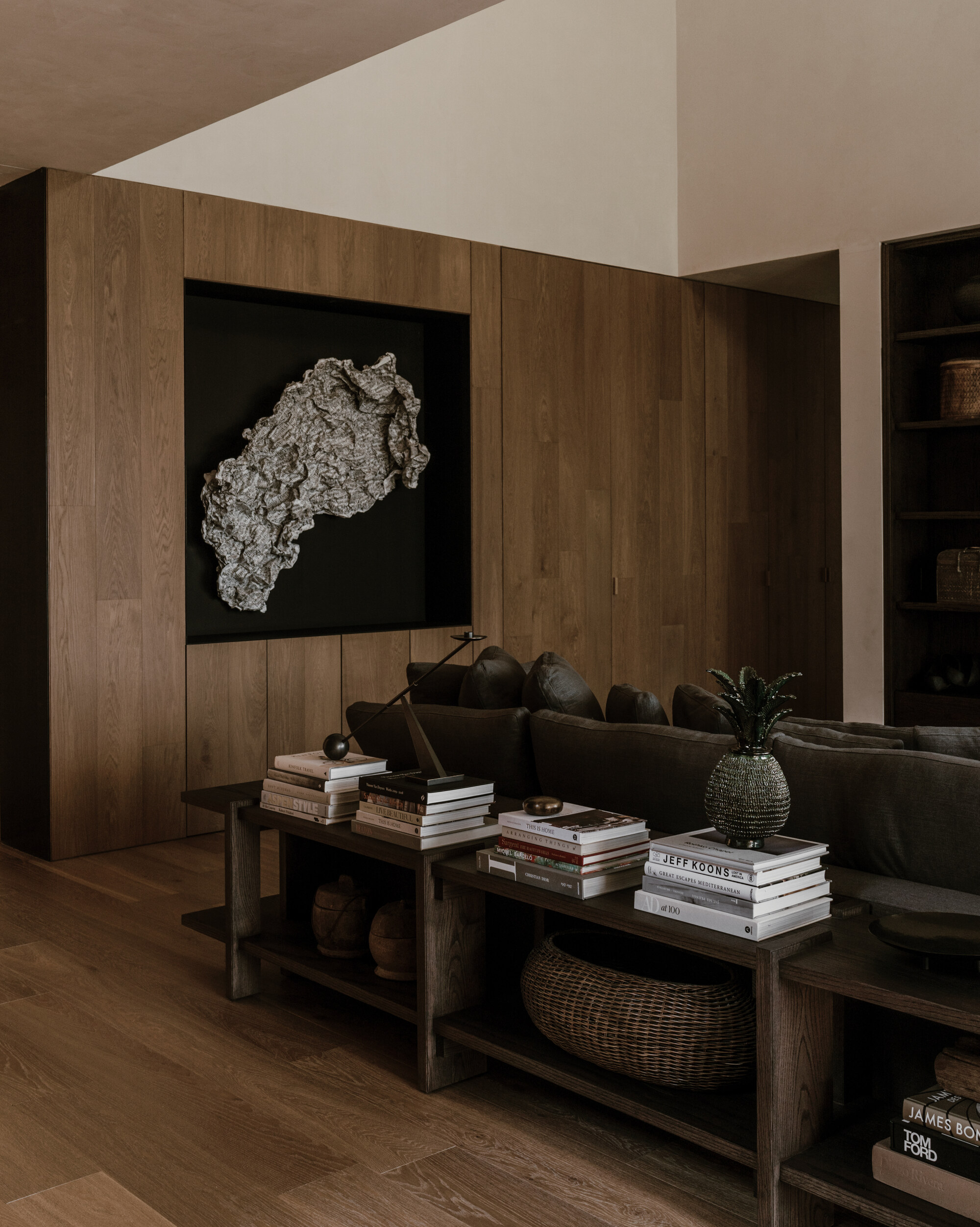Oak-panelled wall with a recessed black niche holding a rough sculpture, above a console stacked with books and a woven basket