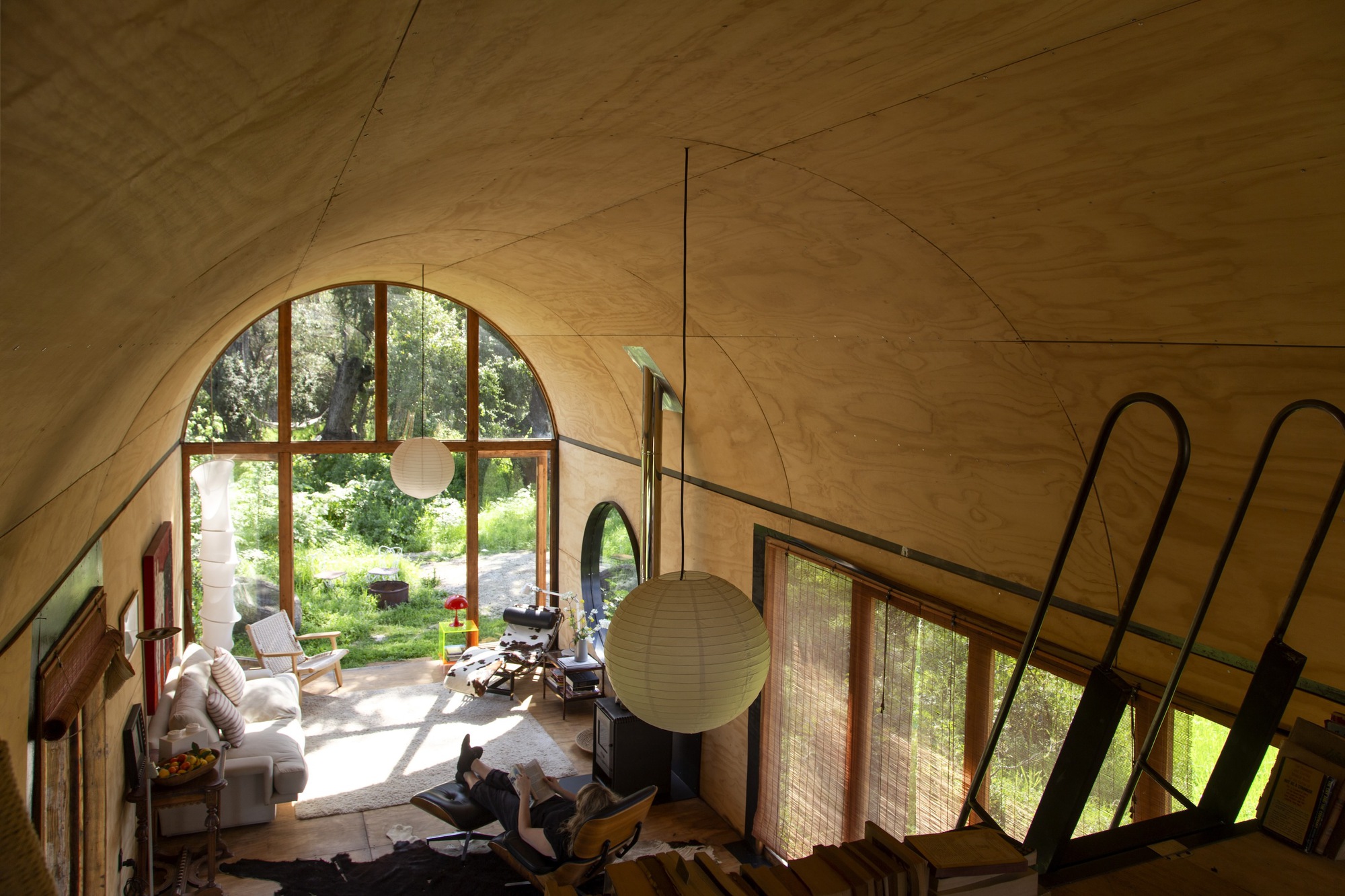 View down from the loft over the plywood vault to a person reclining in a lounge chair near the arched window
