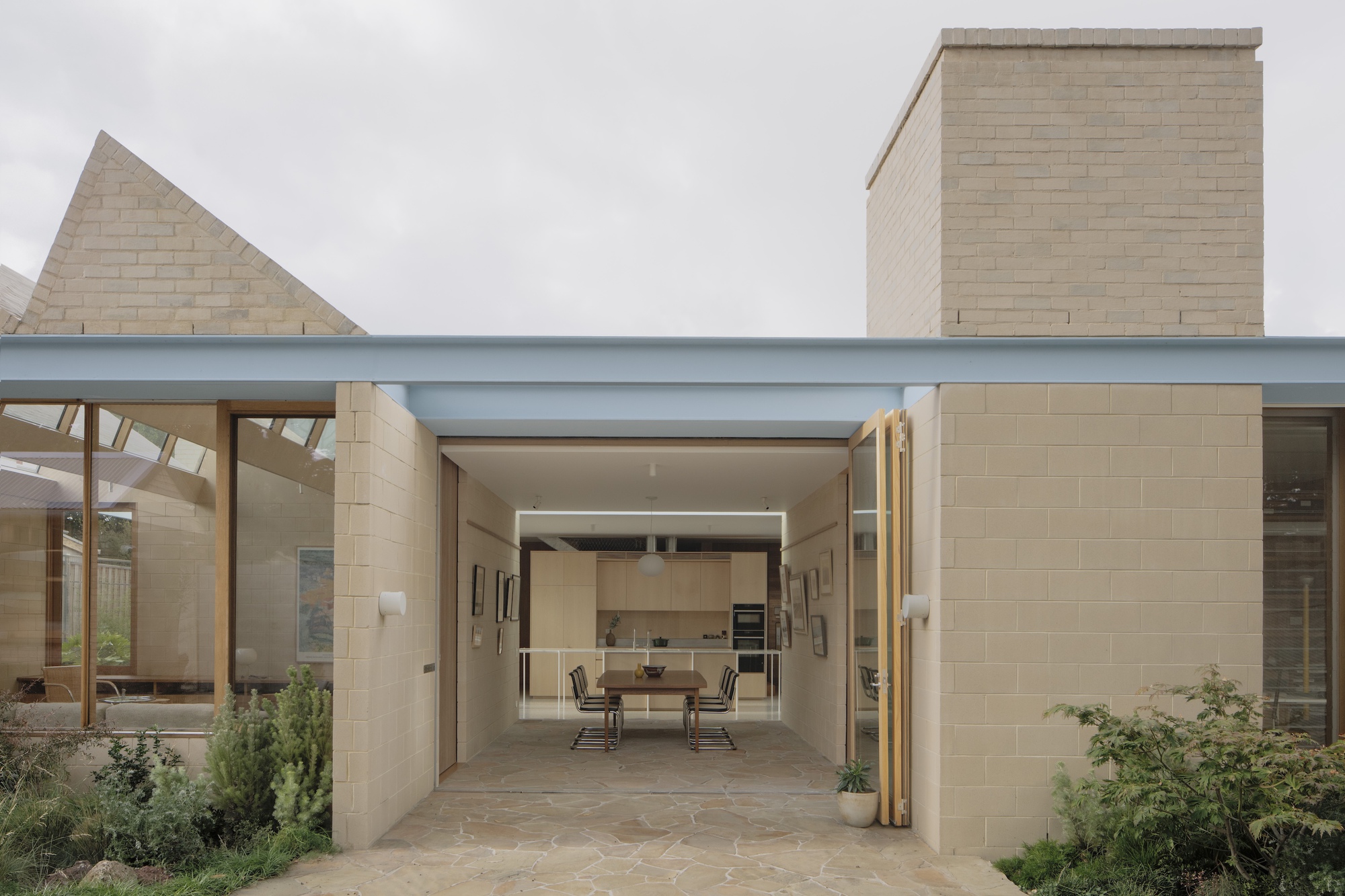 Open entry between pale concrete block walls framing a dining table, with a tall chimney and sawtooth gable under overcast sky