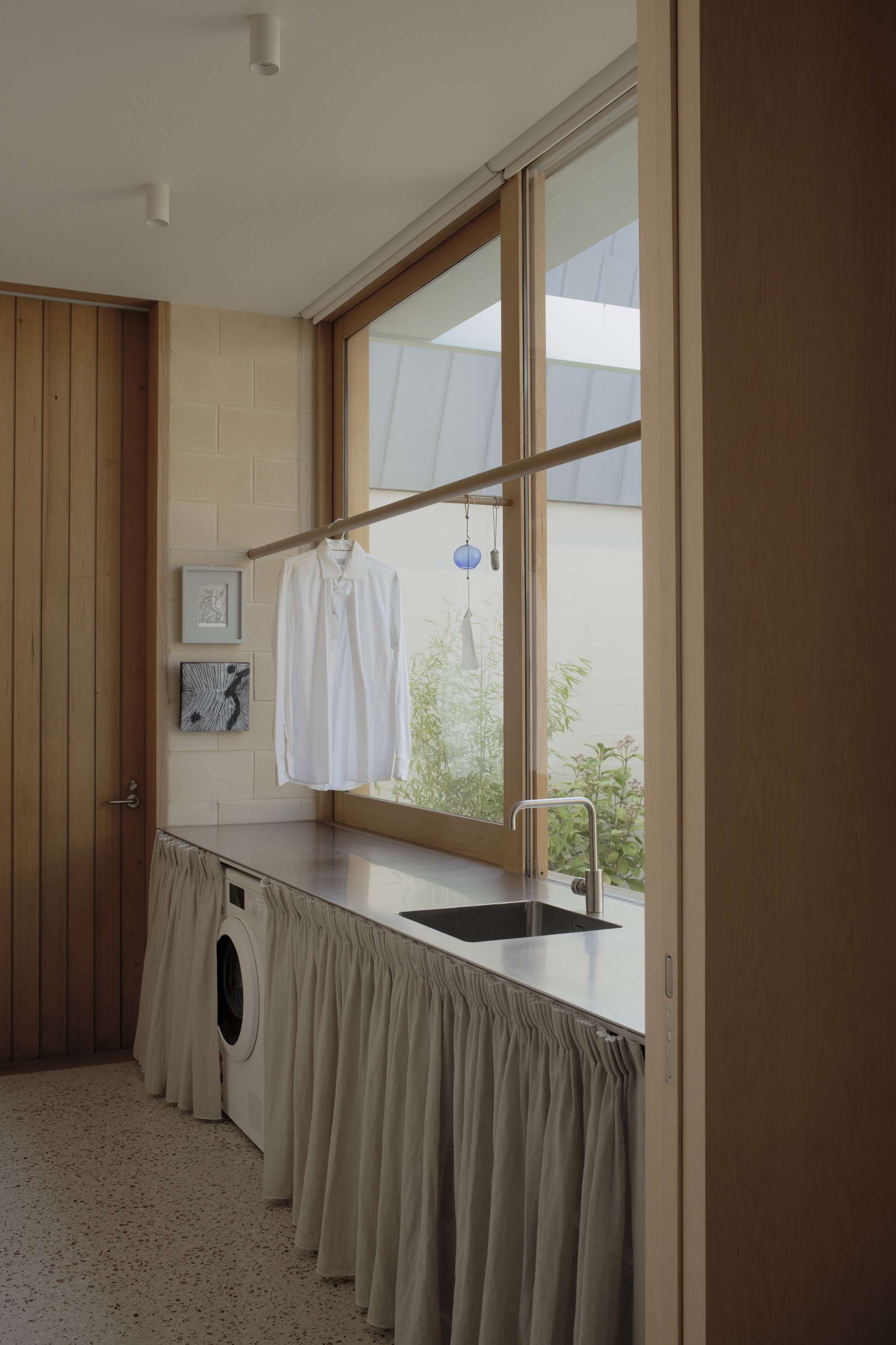 Laundry with a white shirt hanging from a rail at a corner window, linen skirt under the steel bench and sink