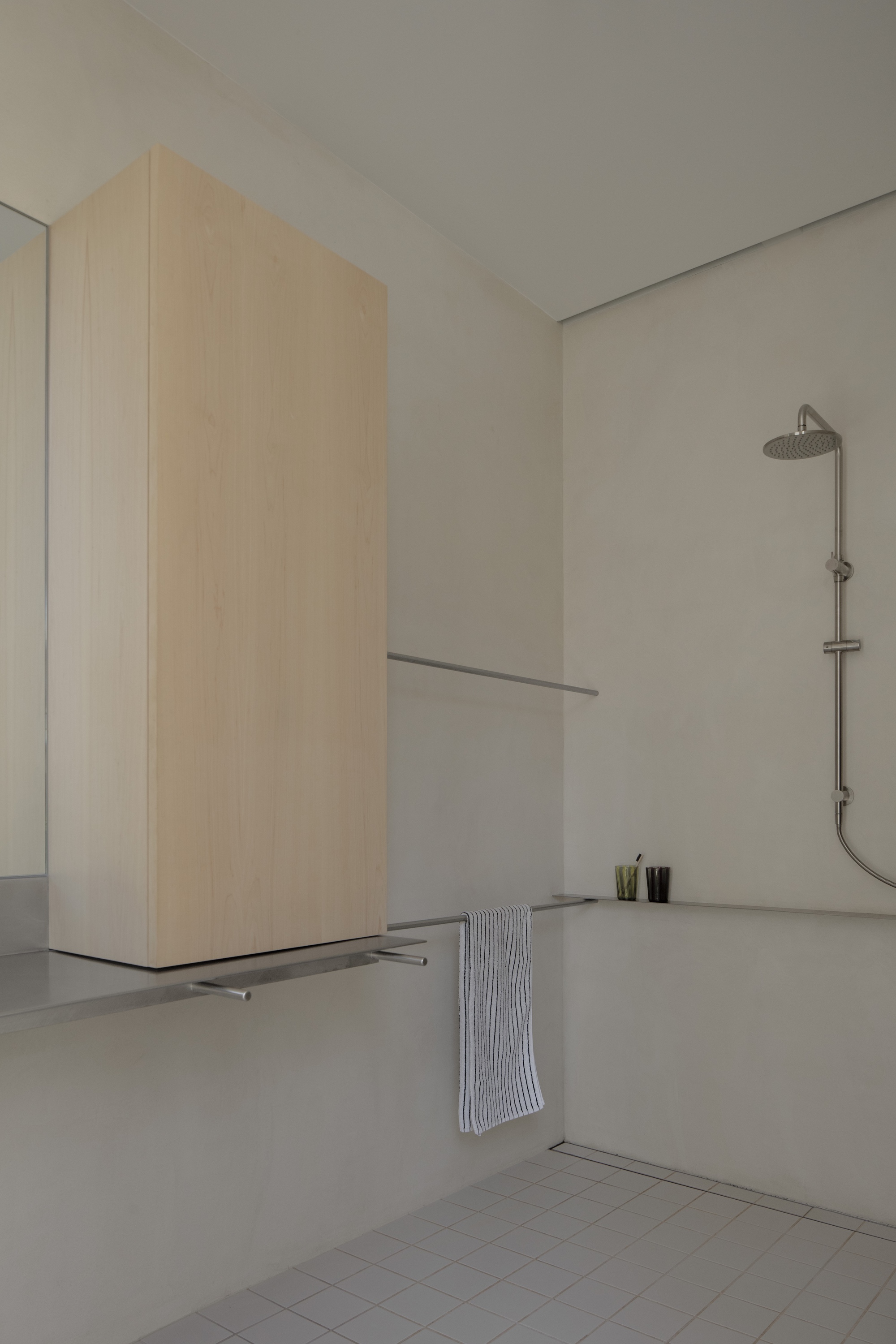 Shower alcove with plastered walls, a pale timber cabinet, steel towel rail and striped towel in soft daylight
