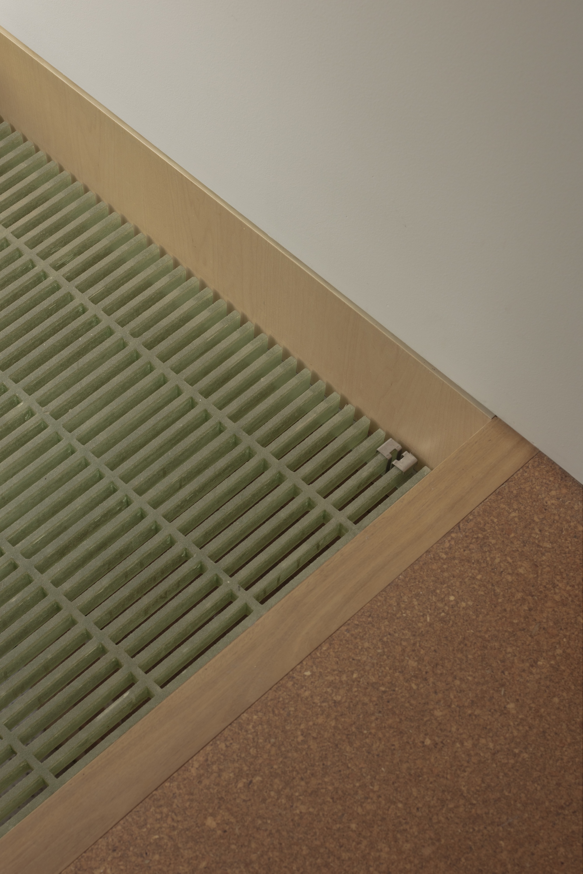 Corner detail of a green fibreglass grating set in a pale timber frame beside a cork floor