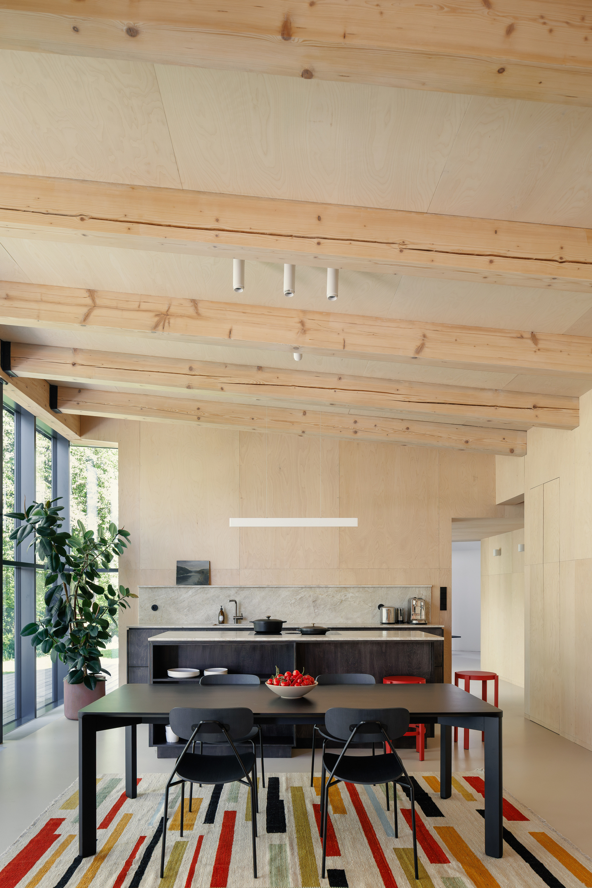 Open kitchen and dining area under exposed timber beams, with a black table, red stools and a striped rug