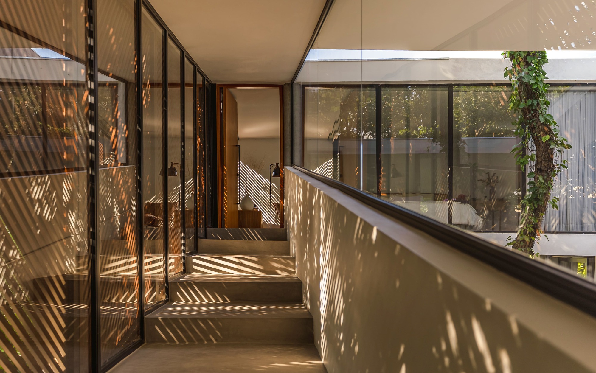 Concrete stair and glazed corridor striped with diagonal shadows from the slatted screen in low afternoon light
