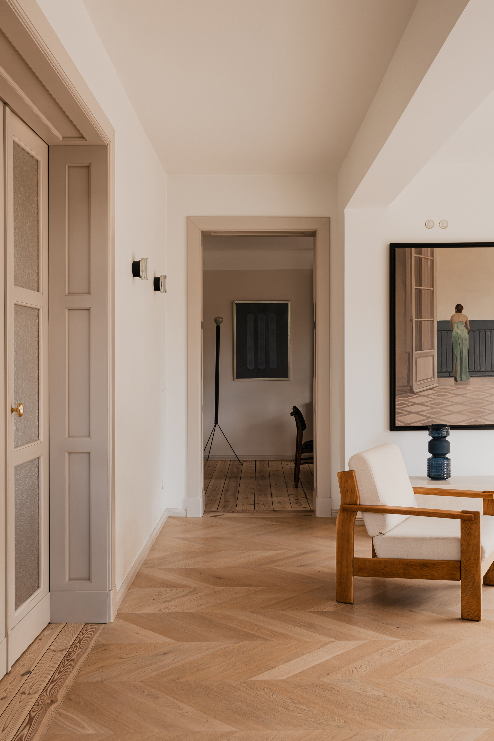 Hallway with herringbone parquet, a paneled door with reeded glass and a framed painting, lit by soft daylight
