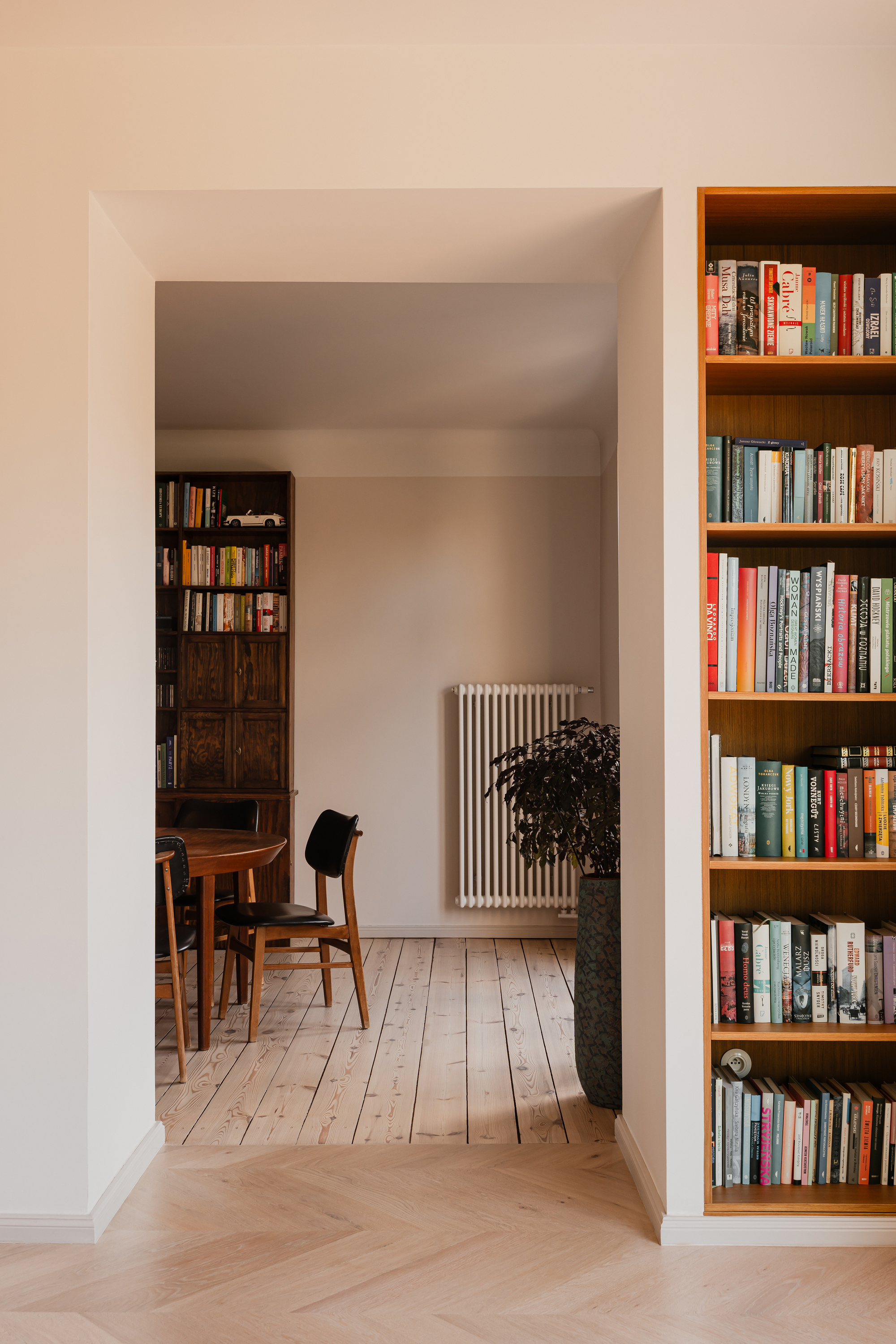 Doorway view through to a dining chair and radiator, framed by a built-in bookshelf and herringbone floor in soft light