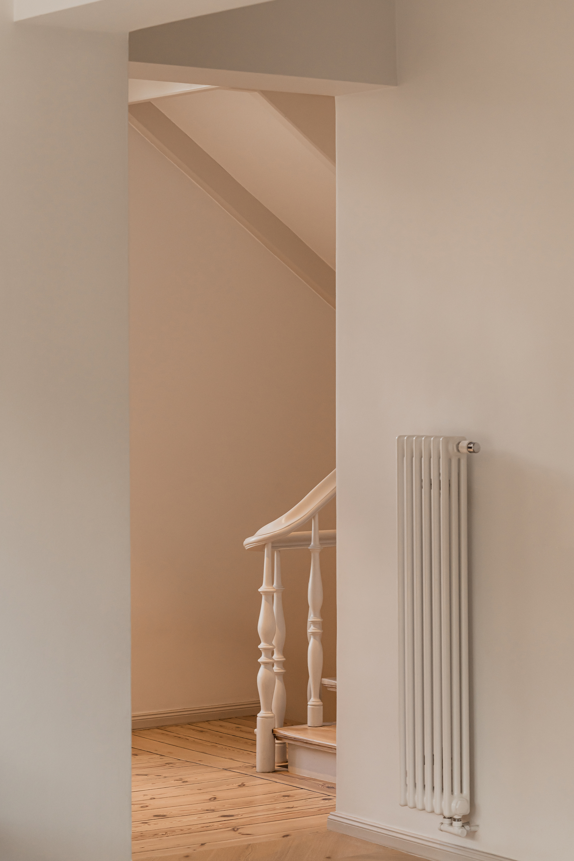 Narrow opening onto a stair landing with a white newel and balusters, a vertical radiator on the adjacent wall