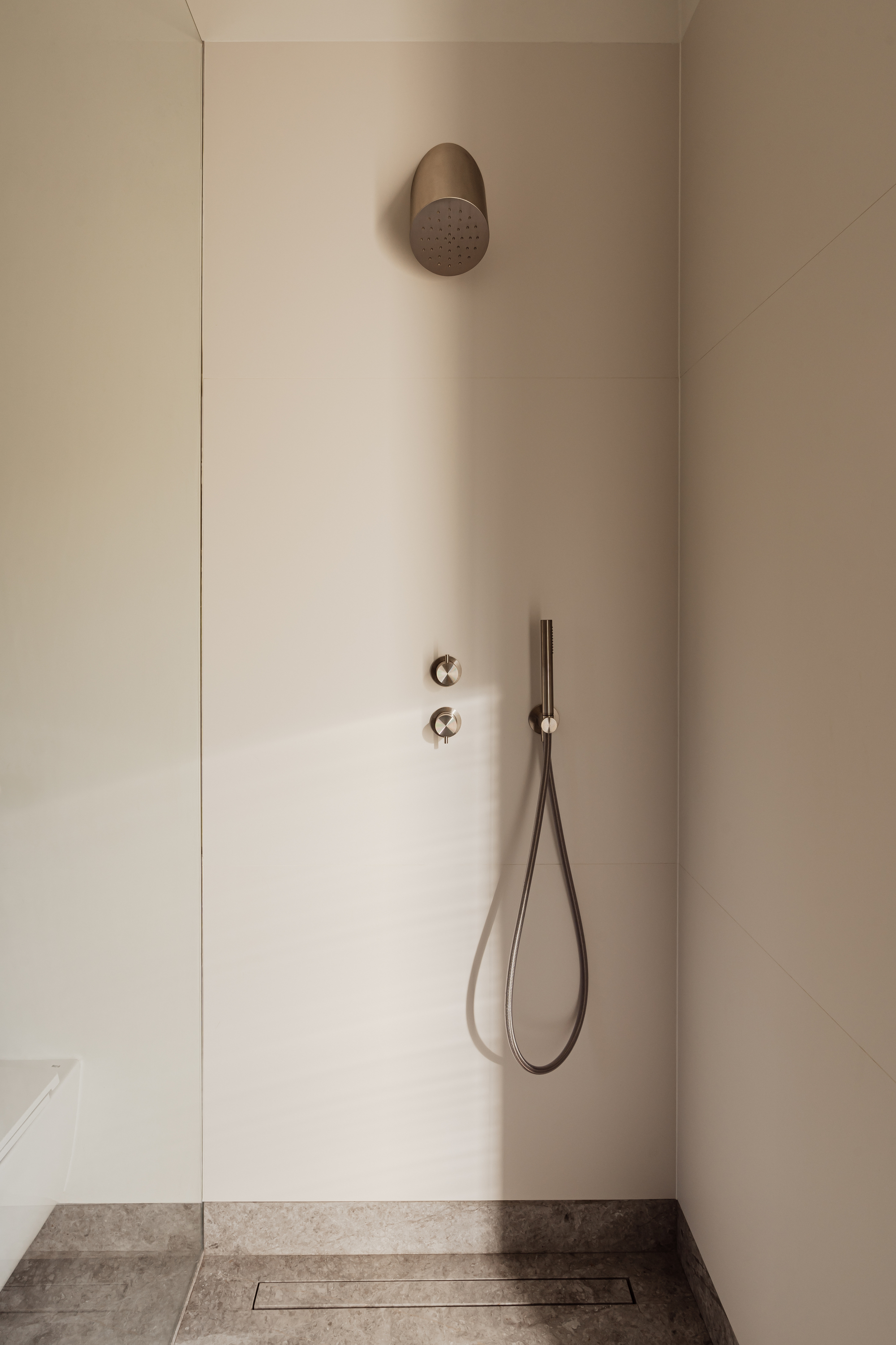 Shower recess with pale panel walls, brushed metal rain head and hand shower, and a linear drain set in grey stone floor