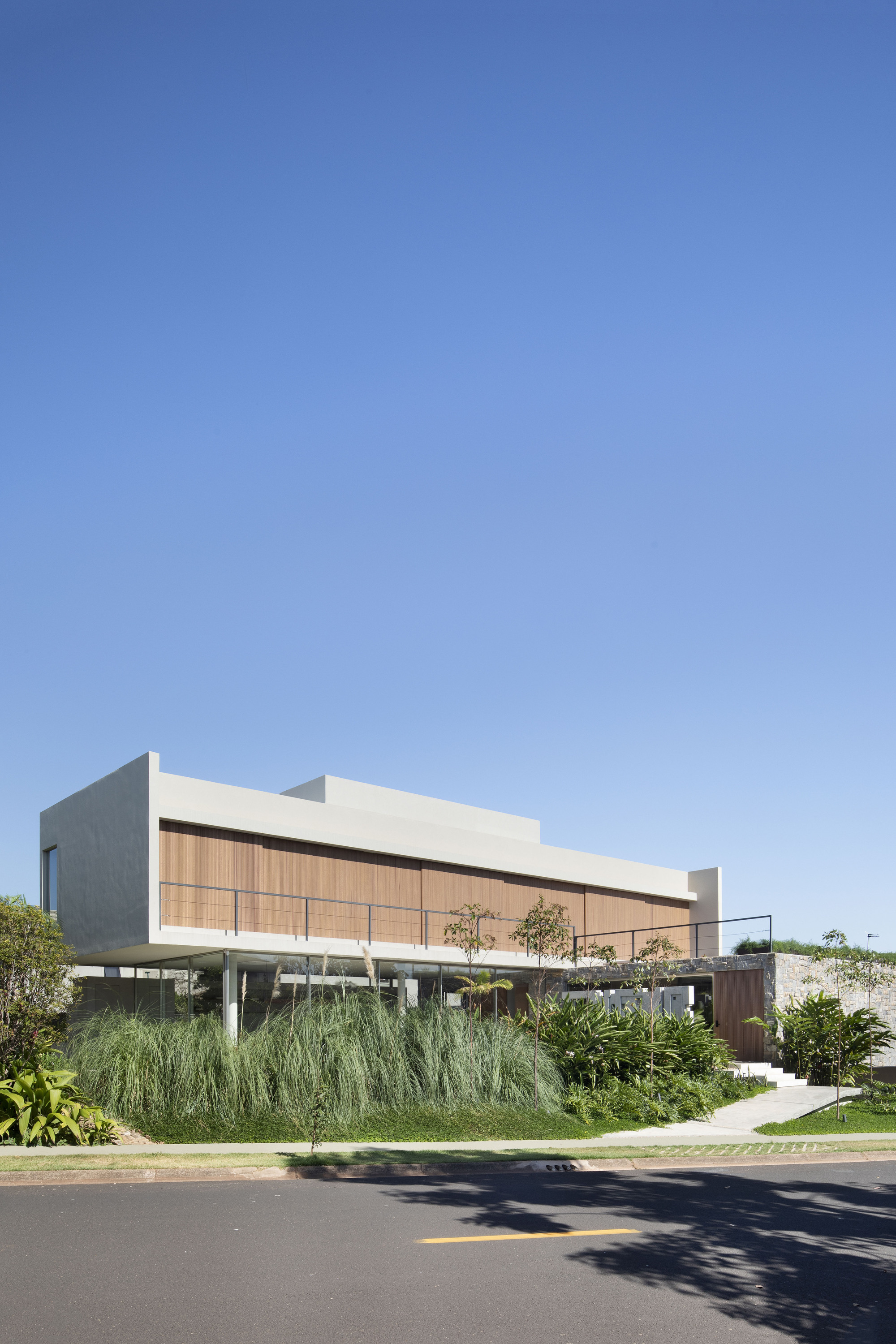 Corner view of the white upper box with timber slat cladding, raised on slim columns above tall grasses in afternoon sun