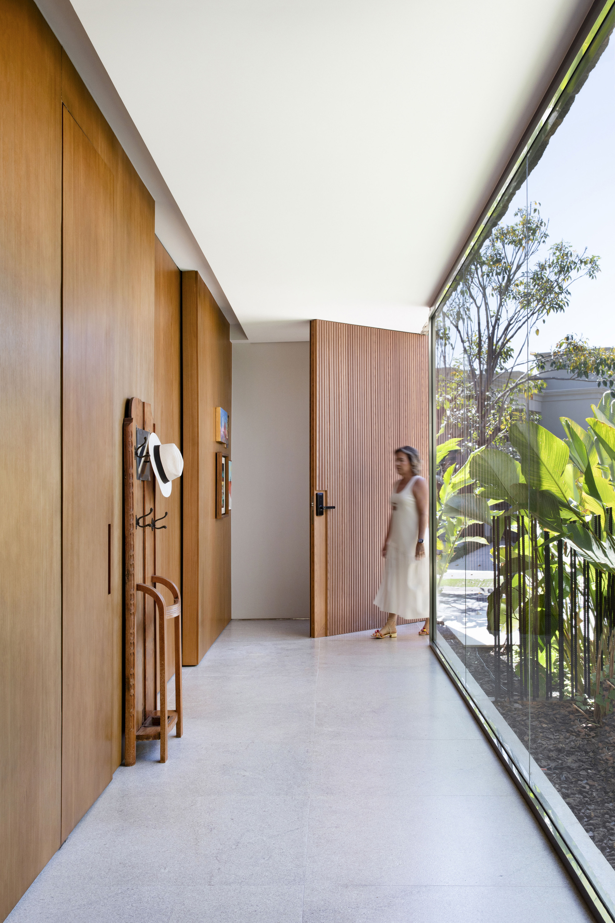 Entry corridor with timber panel walls, a hat on a wooden coat stand and a woman walking beside the glass wall