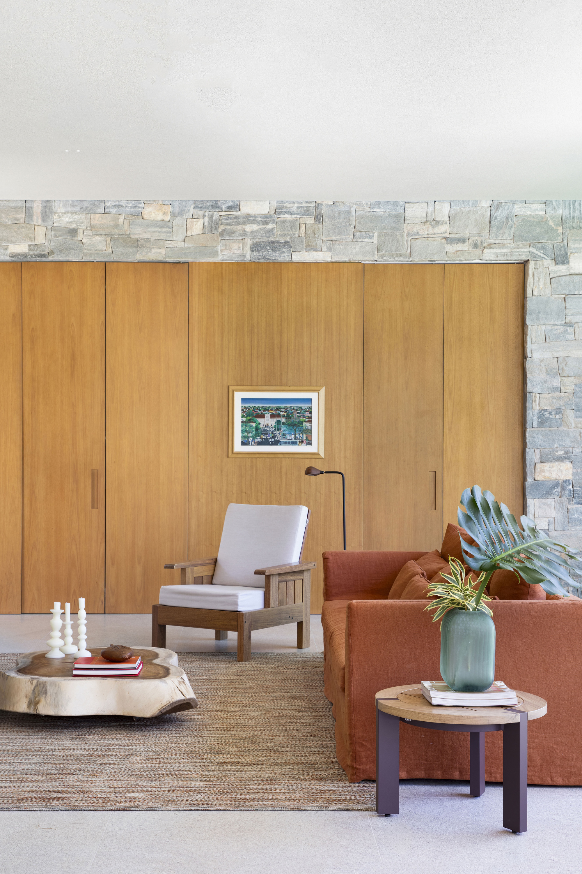 Wood-panelled wall with a small framed painting beside a stone return, above a rust sofa, armchair and tree-trunk coffee table