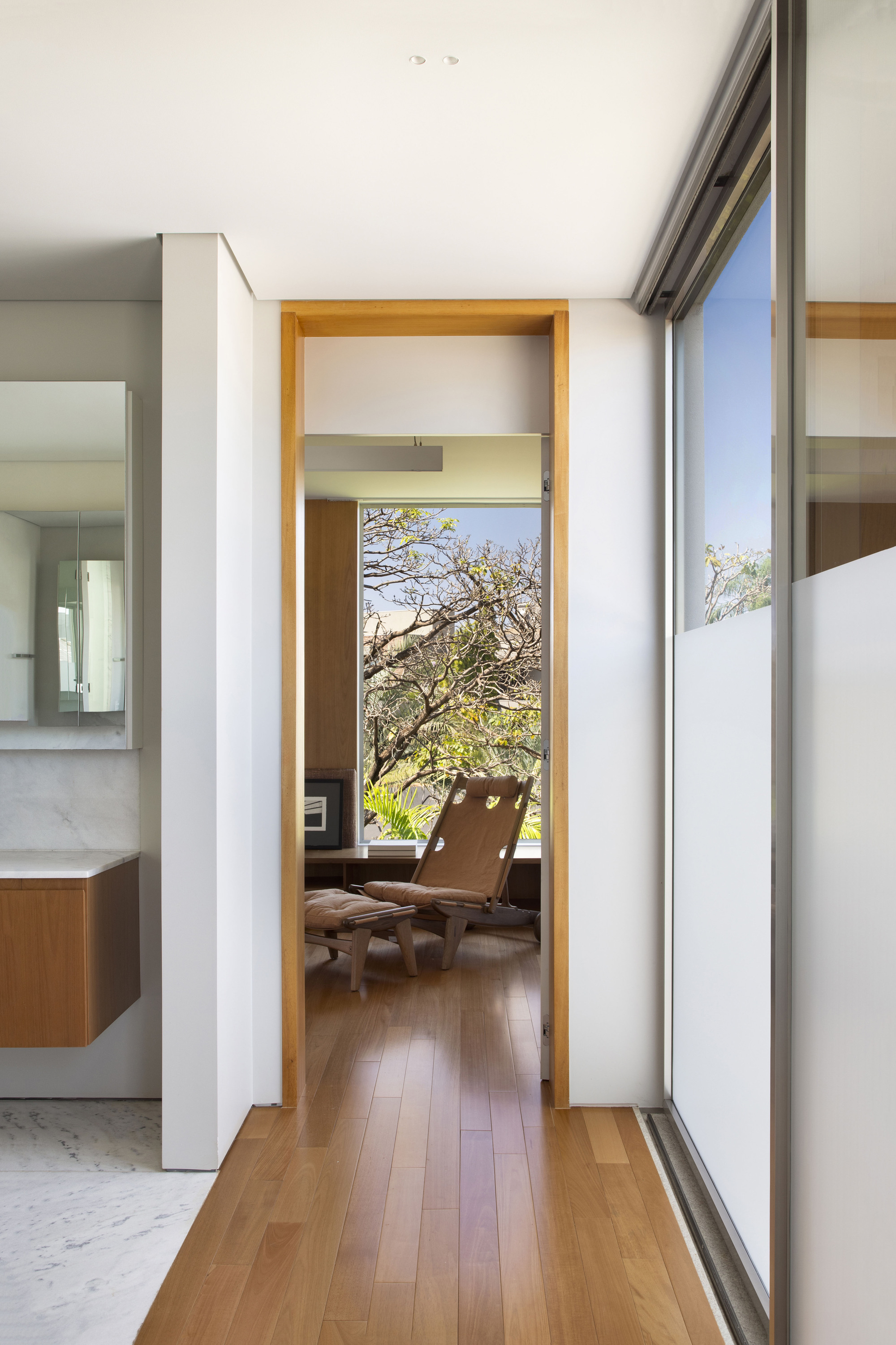 Timber-framed doorway looking from a bathroom into a sitting room, with a frosted glass sliding door and tree beyond