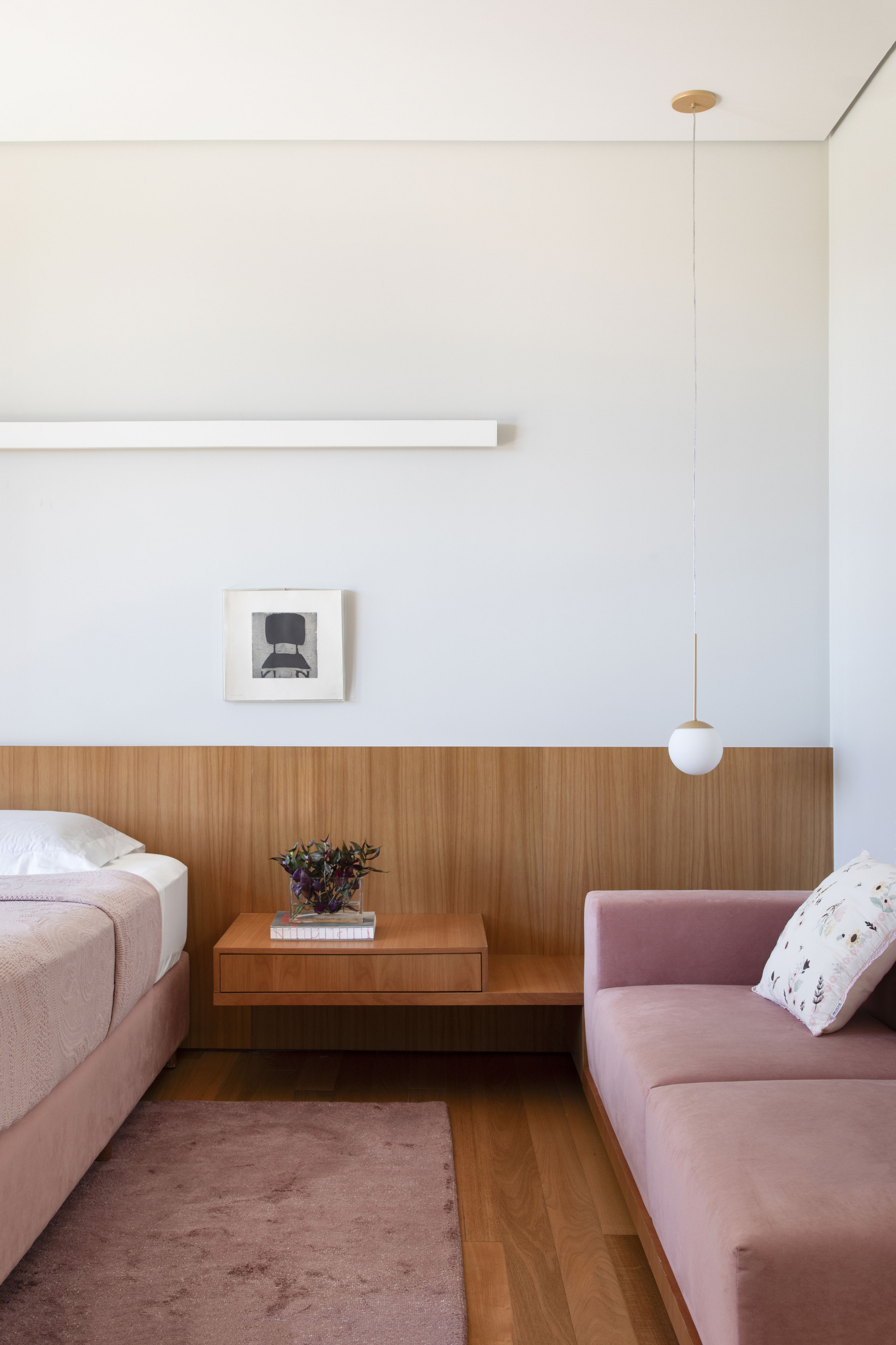 Bedroom corner with a floating timber nightstand, pink velvet sofa and a globe pendant lamp in soft daylight