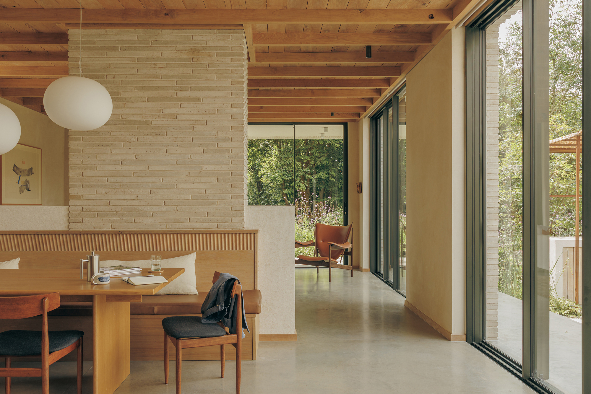 Dining area with built-in timber bench, brick column and exposed beam ceiling opening through sliding glass doors to the garden