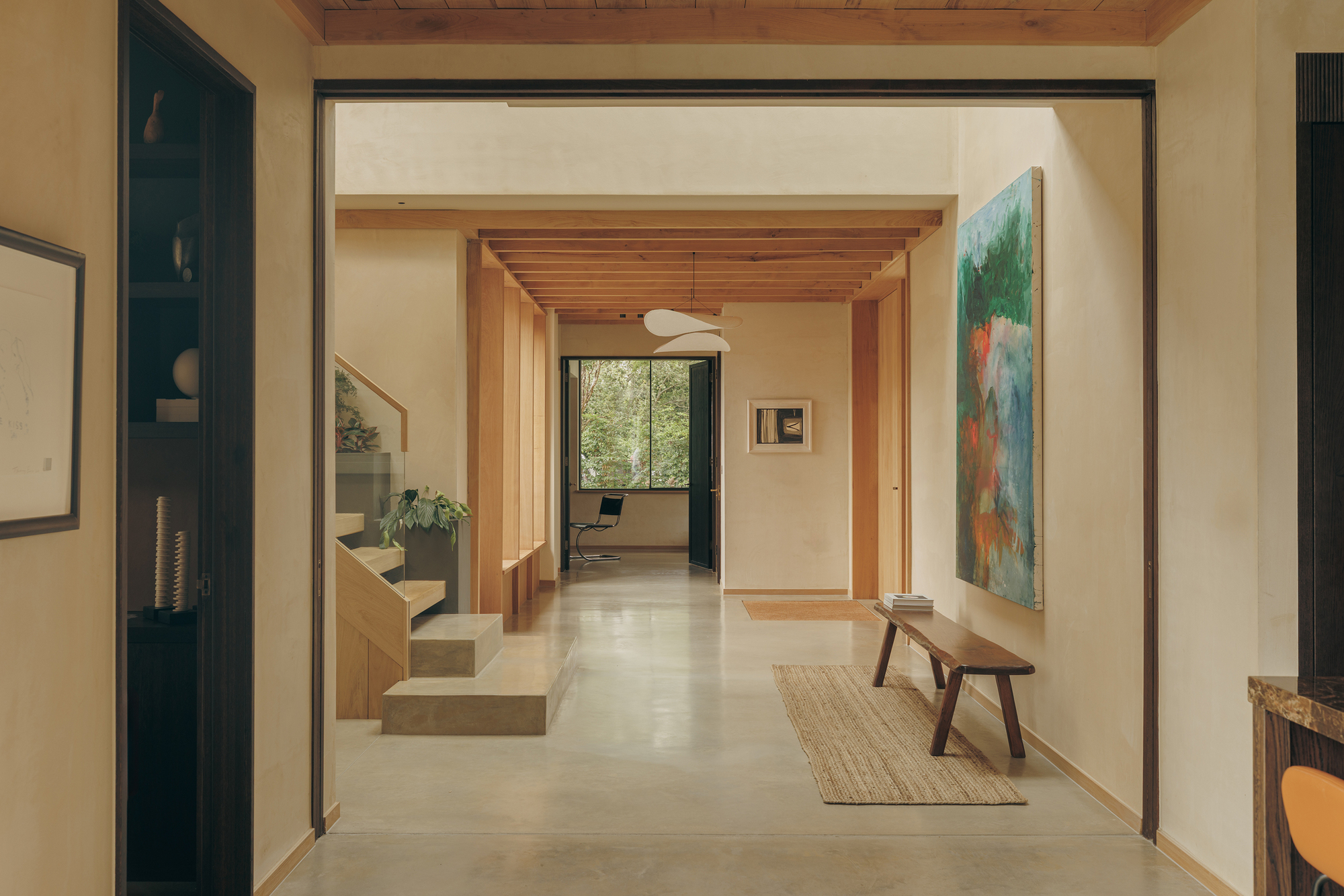 Entry hallway with timber ceiling beams, a floating concrete stair and a large abstract painting above a wooden bench