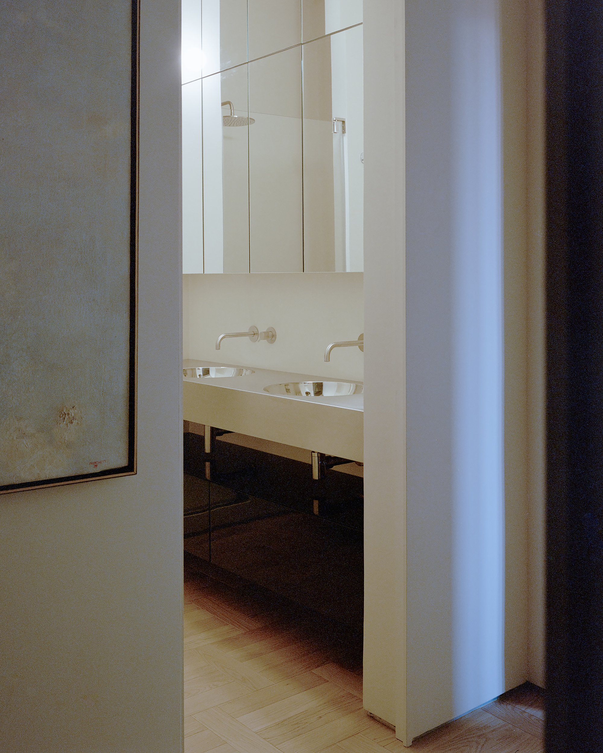 Doorway view of a double basin vanity with wall-mounted taps and mirrored cabinets above a herringbone timber floor