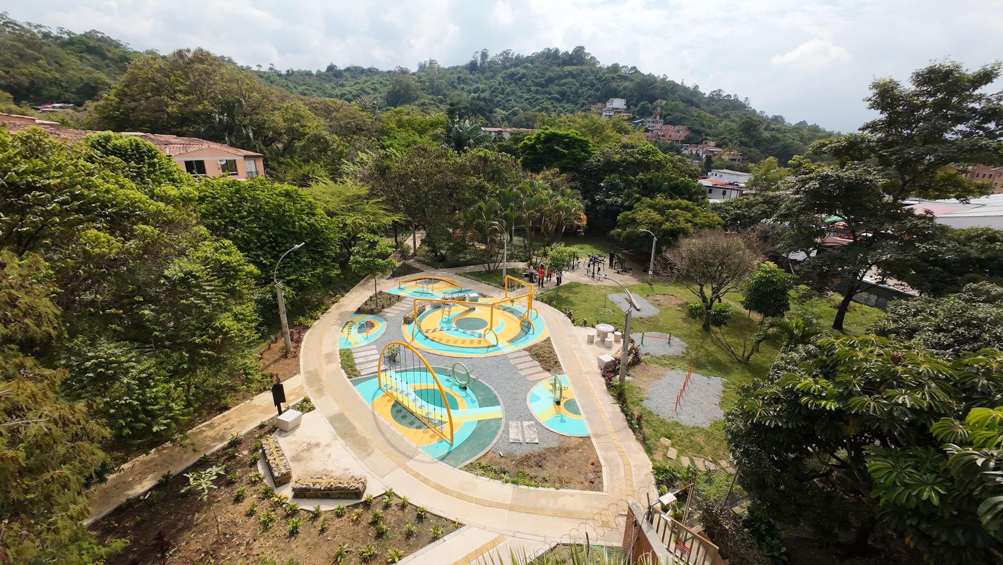 Elevated view of curved paths and yellow play arches on colored flooring, with forested hills under an overcast sky