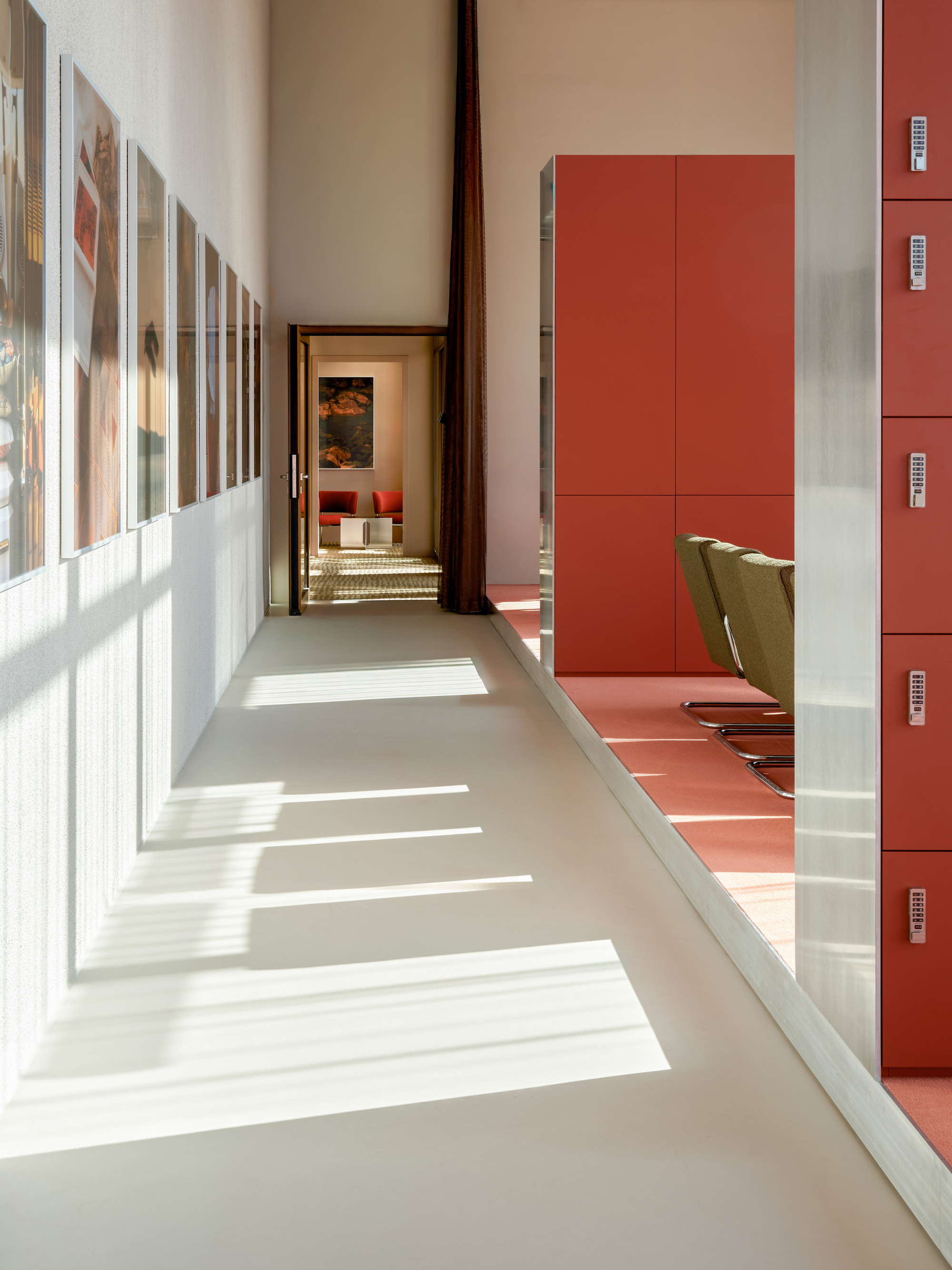 Corridor with framed prints on the left and orange locker doors on the right, striped with sunlight across the floor