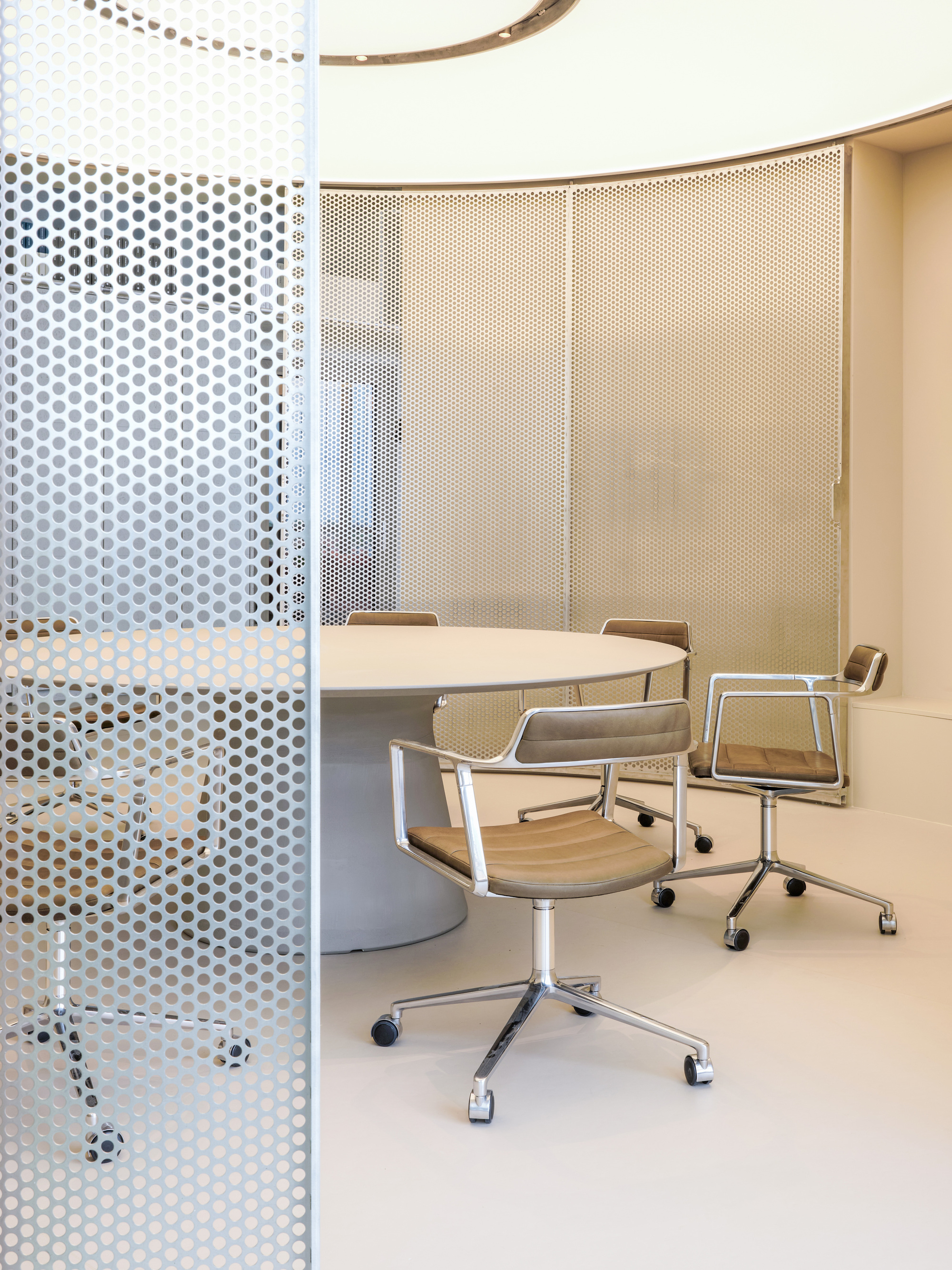Round table and chrome-framed chairs inside a curved room, with a perforated metal screen in the foreground