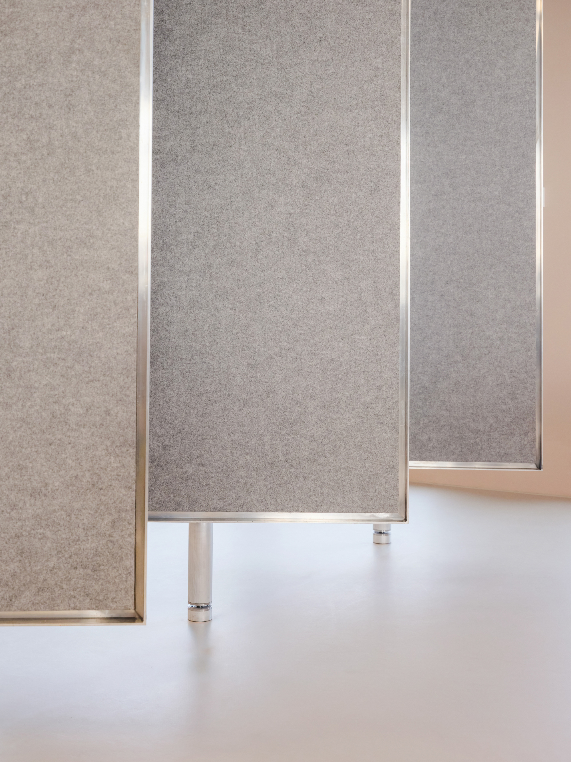 Grey felt acoustic panels in steel frames standing on cylindrical metal feet above a pale floor in soft daylight