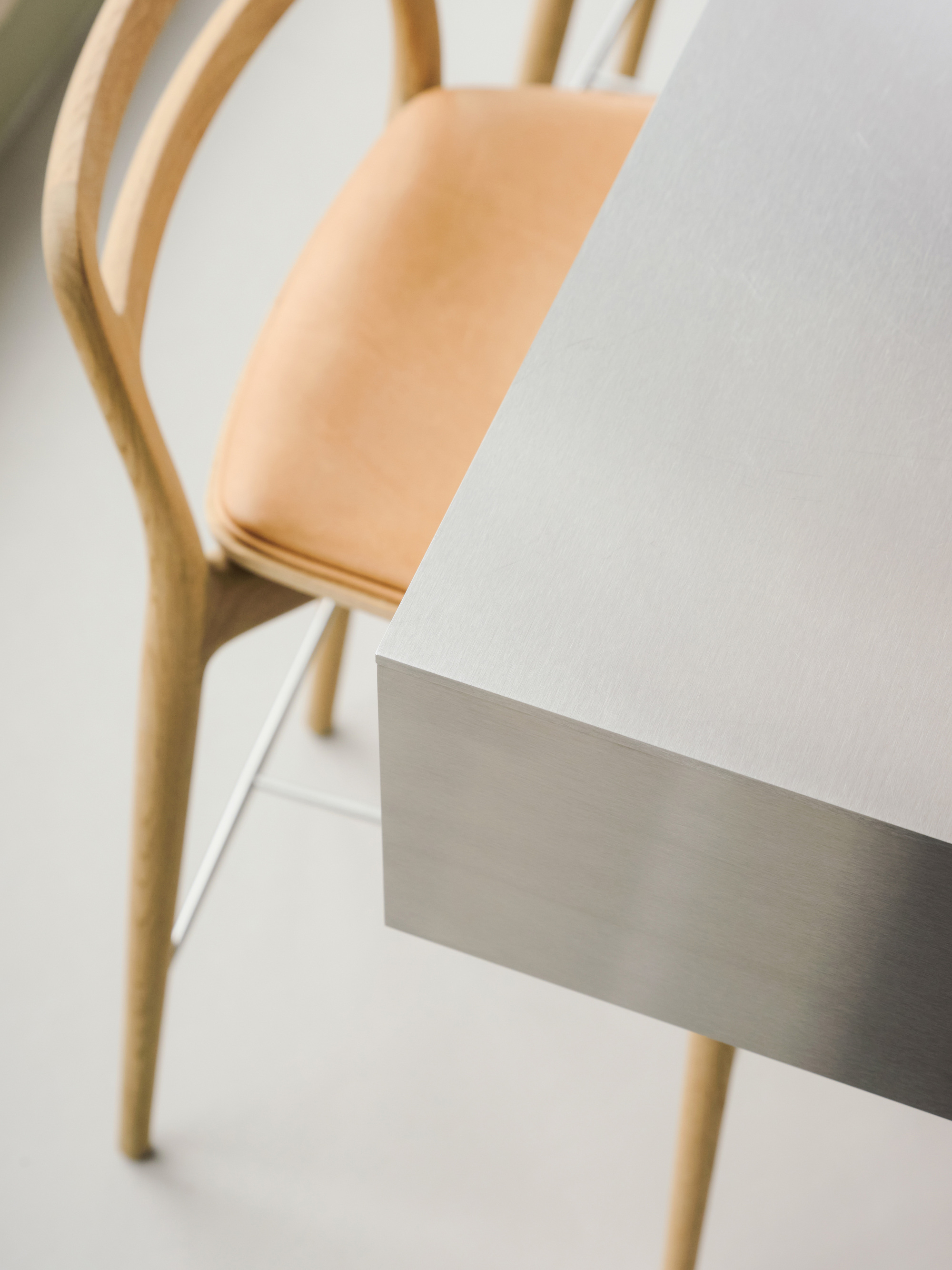 Close-up of a brushed steel counter corner beside an oak bar stool with a tan leather seat