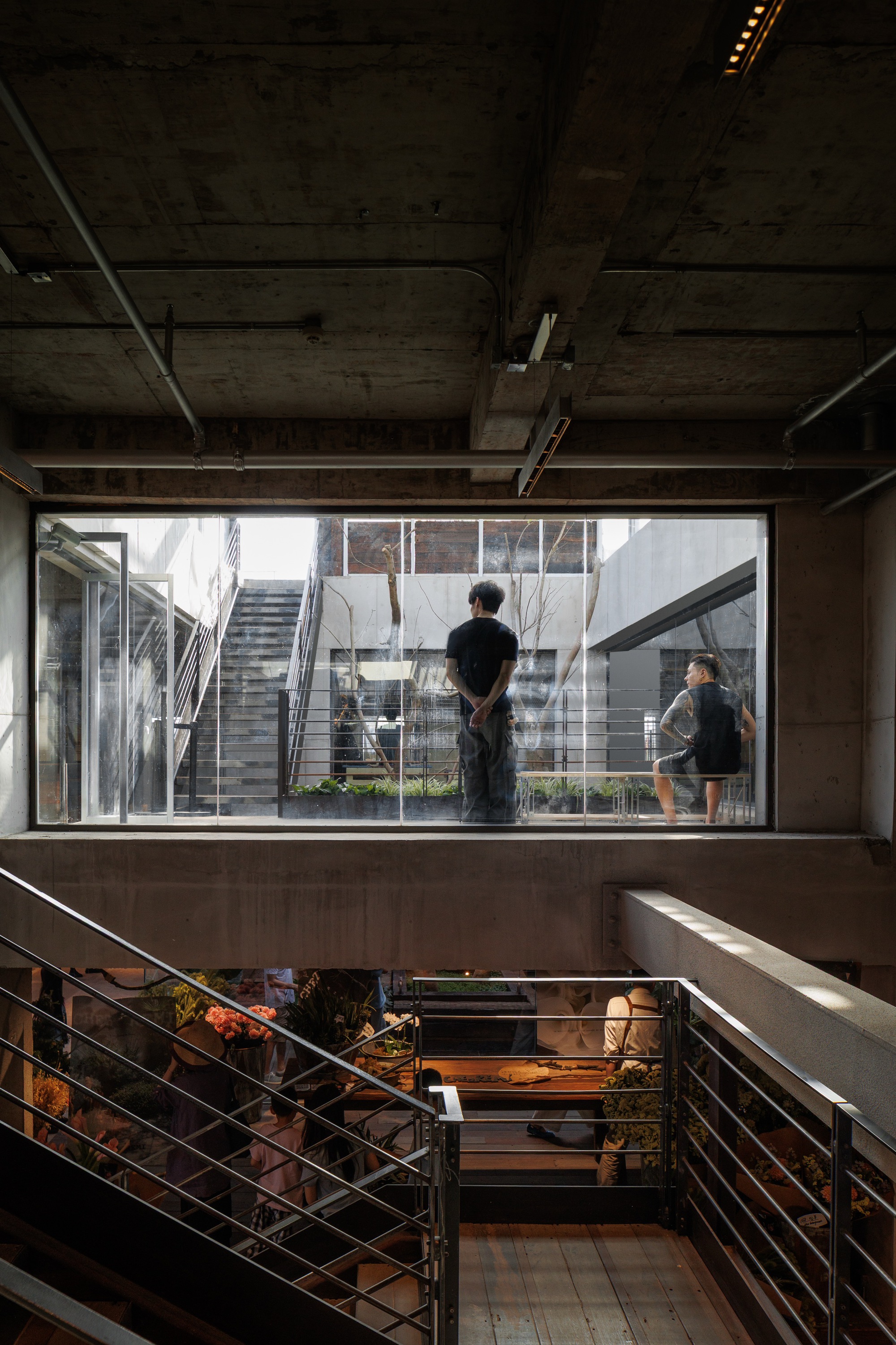 Concrete-framed window looking out to an exterior stair and two standing figures, above a steel-railed stairwell