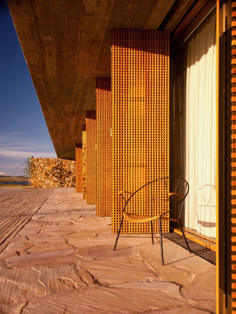 Close view of timber lattice panels beside a curtained glass door, with a single chair on flagstone paving in warm evening sun