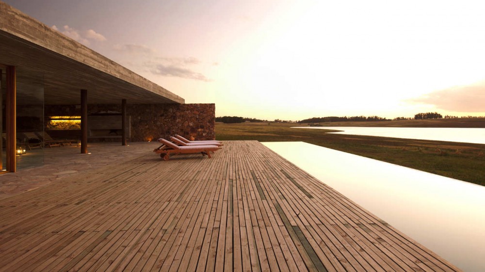 Timber deck with wooden loungers beside an infinity edge pool, under a board-formed concrete roof at sunset