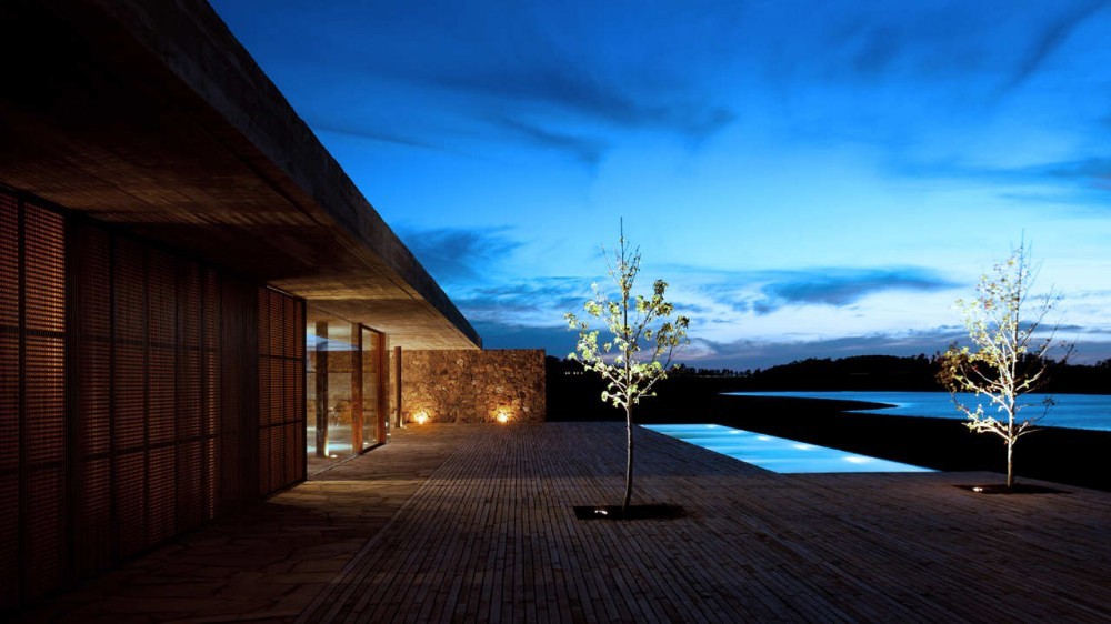 Slatted timber screen wall and stone end wall beside a lit deck and pool at blue hour