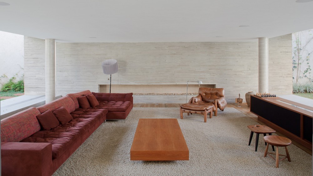 Living room with a long burgundy tufted sofa, low timber coffee table and leather armchair on a shaggy cream rug