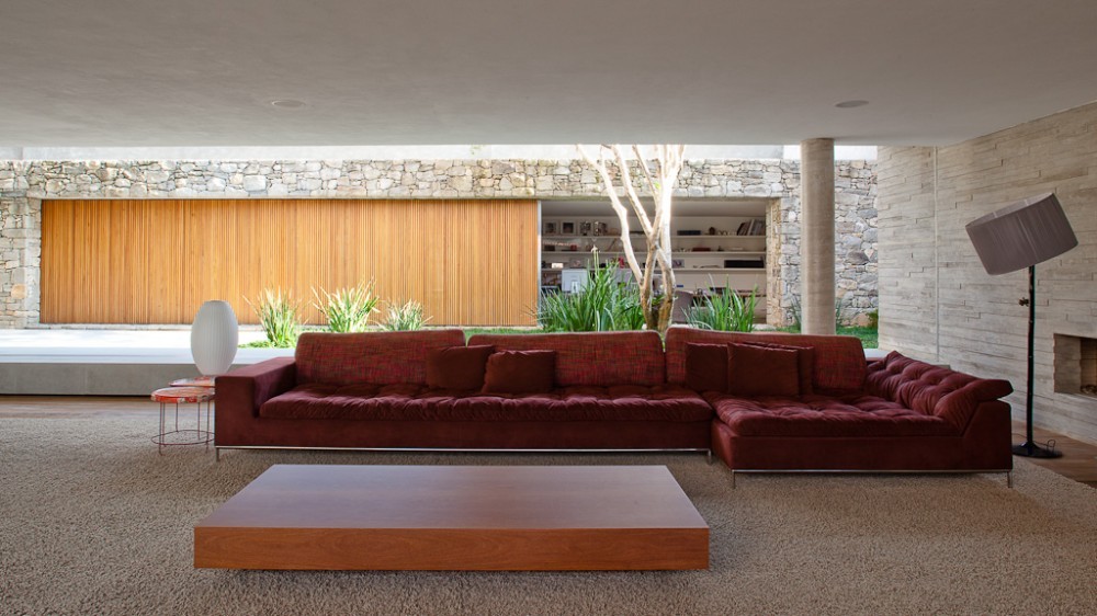 Burgundy sectional sofa facing a garden courtyard with a slim tree, grasses and a timber-slatted panel in a stone wall