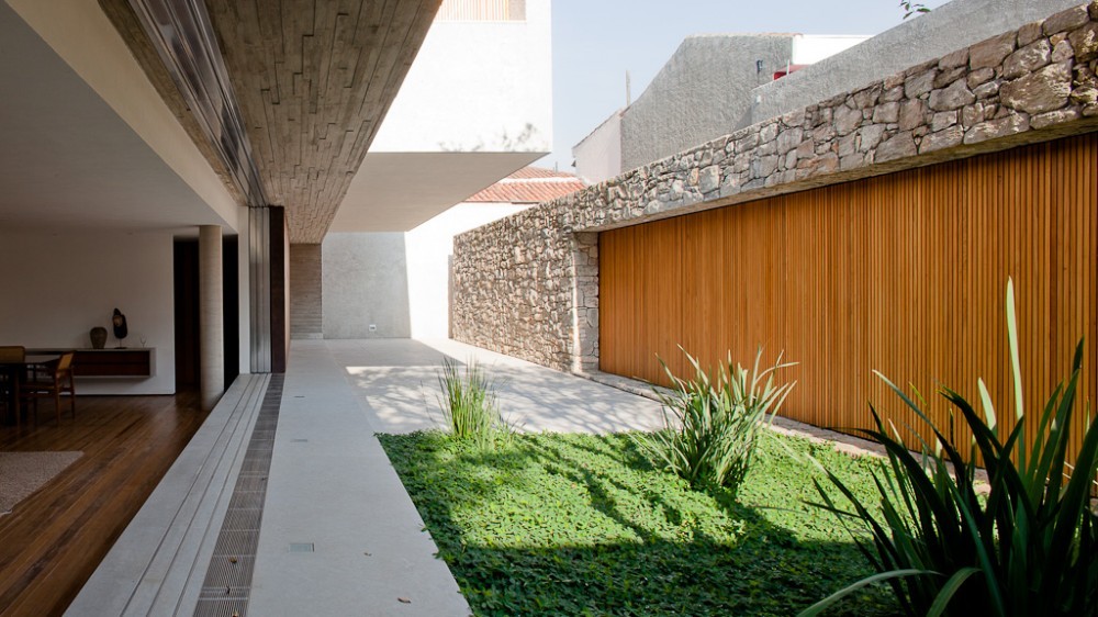 Side courtyard with a lawn, agave plants and a stone wall with vertical timber slats in dappled afternoon sun