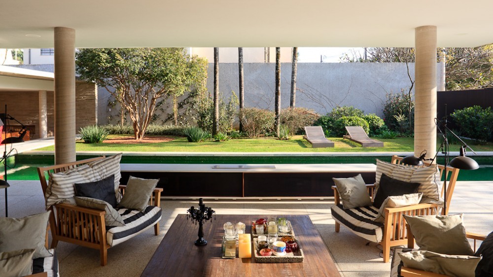 Covered terrace with striped teak armchairs and a coffee table, looking past round columns to a green pool and lawn