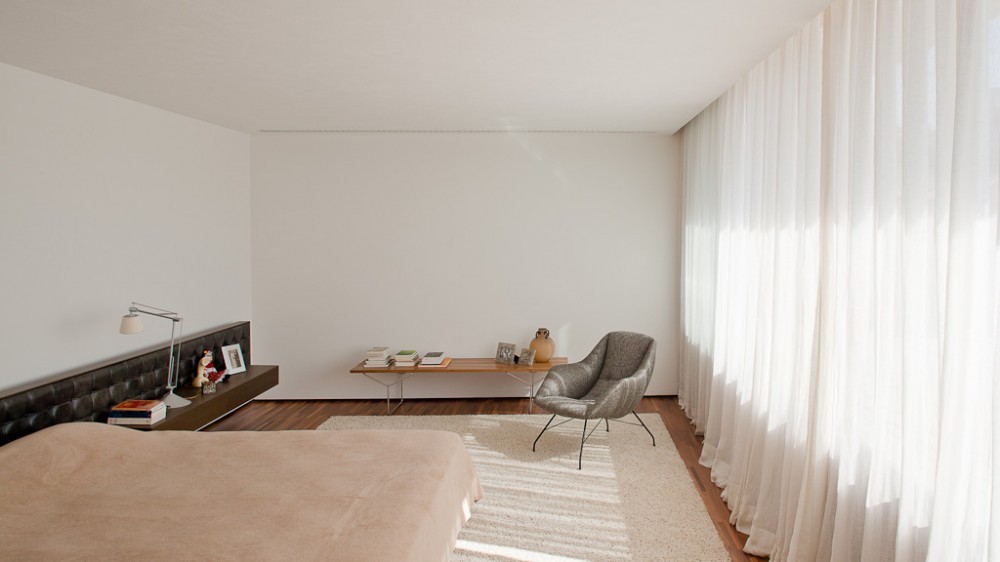 Bedroom with a tufted leather headboard, a timber bench and a grey armchair beside sunlit sheer curtains