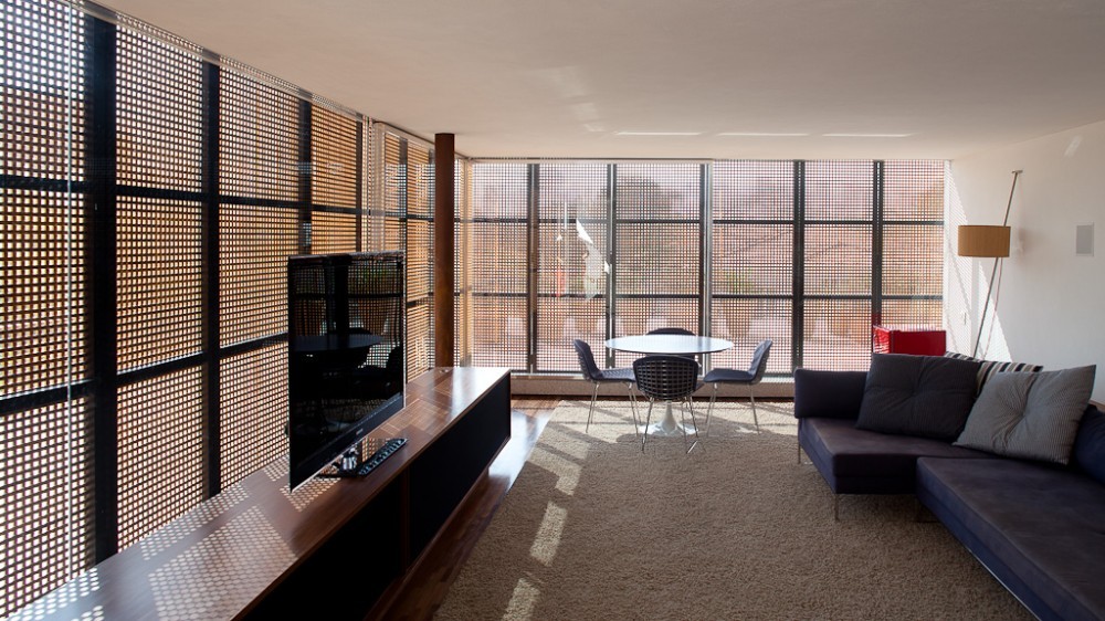 Living room with perforated screen walls casting dotted light across a rug, dining table and low blue sofa