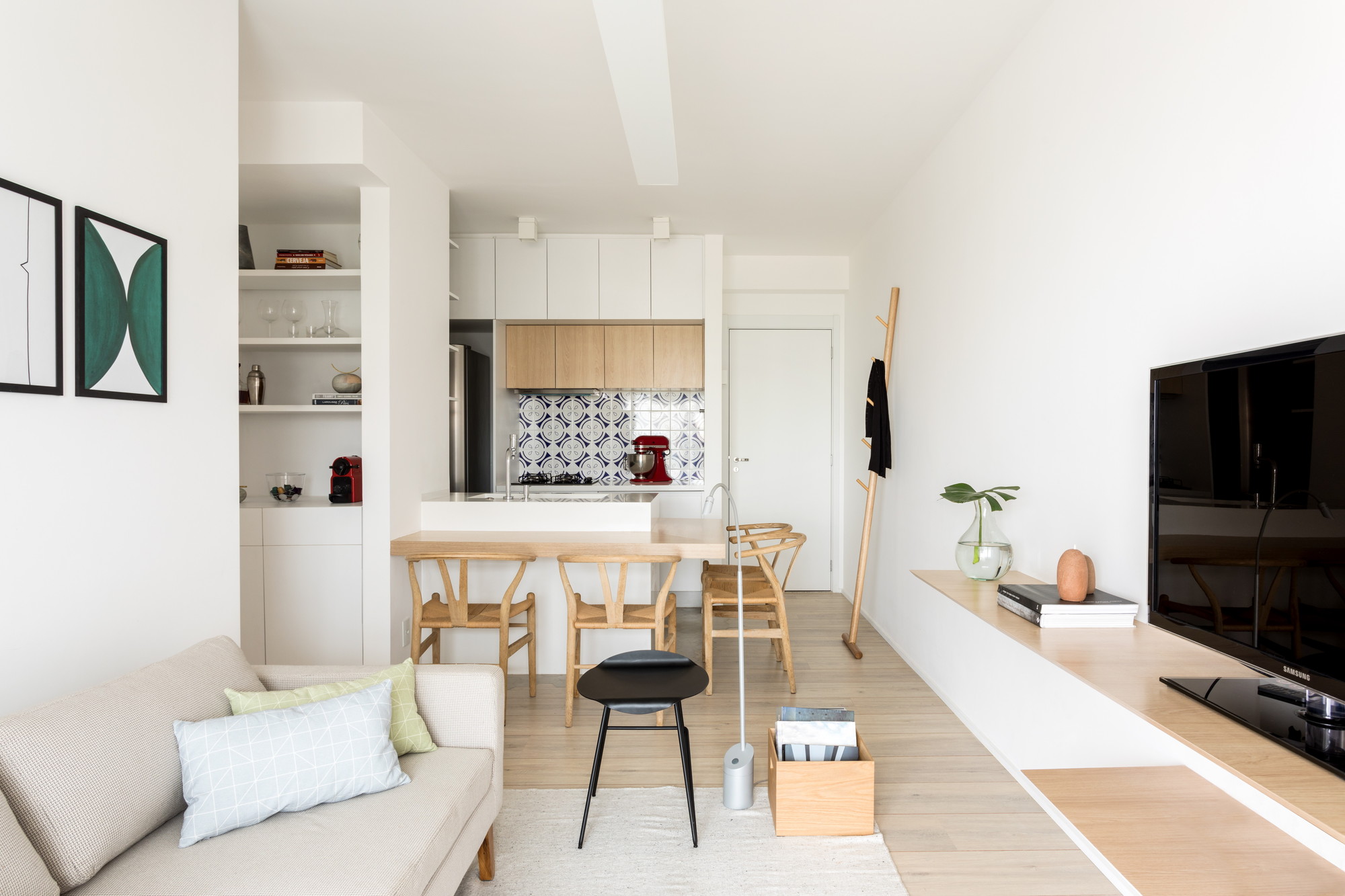 Living room looking toward the open kitchen, with a beige sofa, wishbone chairs and a long oak shelf under daylight